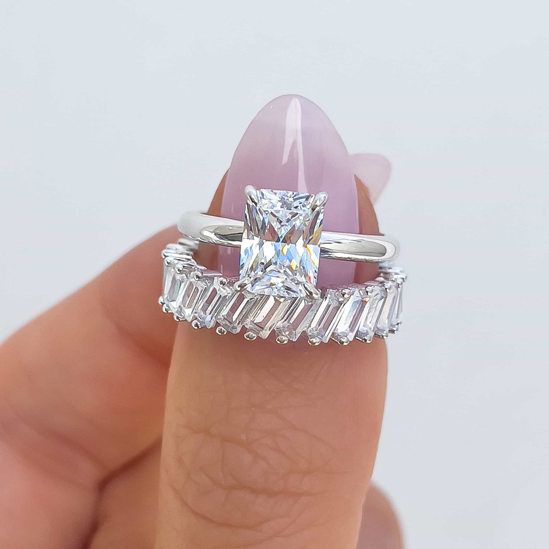 Silver 1.5 carat radiant cut solitaire paired with silver baguette band on model with light pink nails