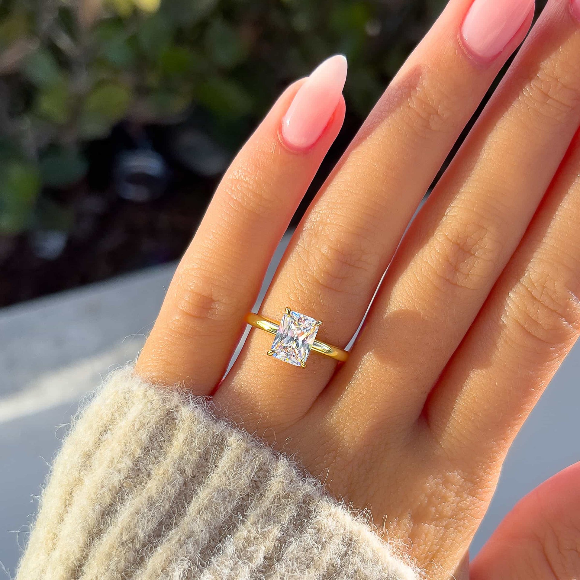 Classic gold 1.5 carat radiant cut solitaire engagement ring on model with tan sweater