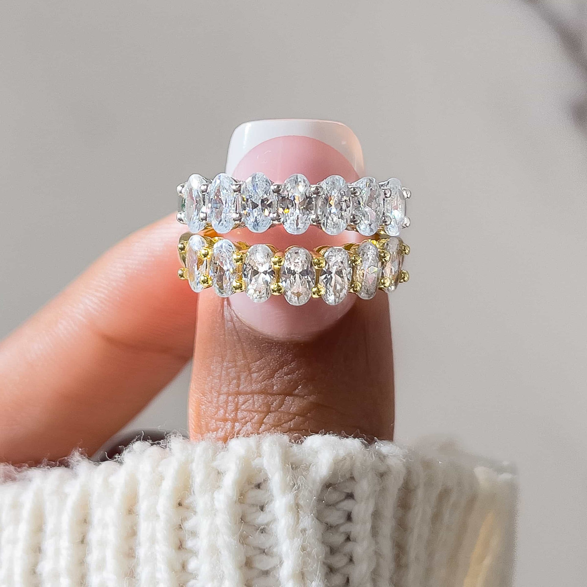 gold and silver oval cut half eternity wedding bands on model's hand with cream sweater