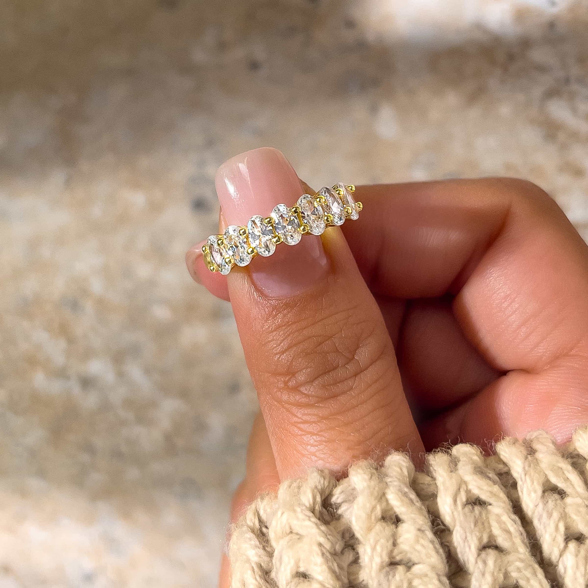 gold oval cut half eternity wedding band on model's hand with tan sweater