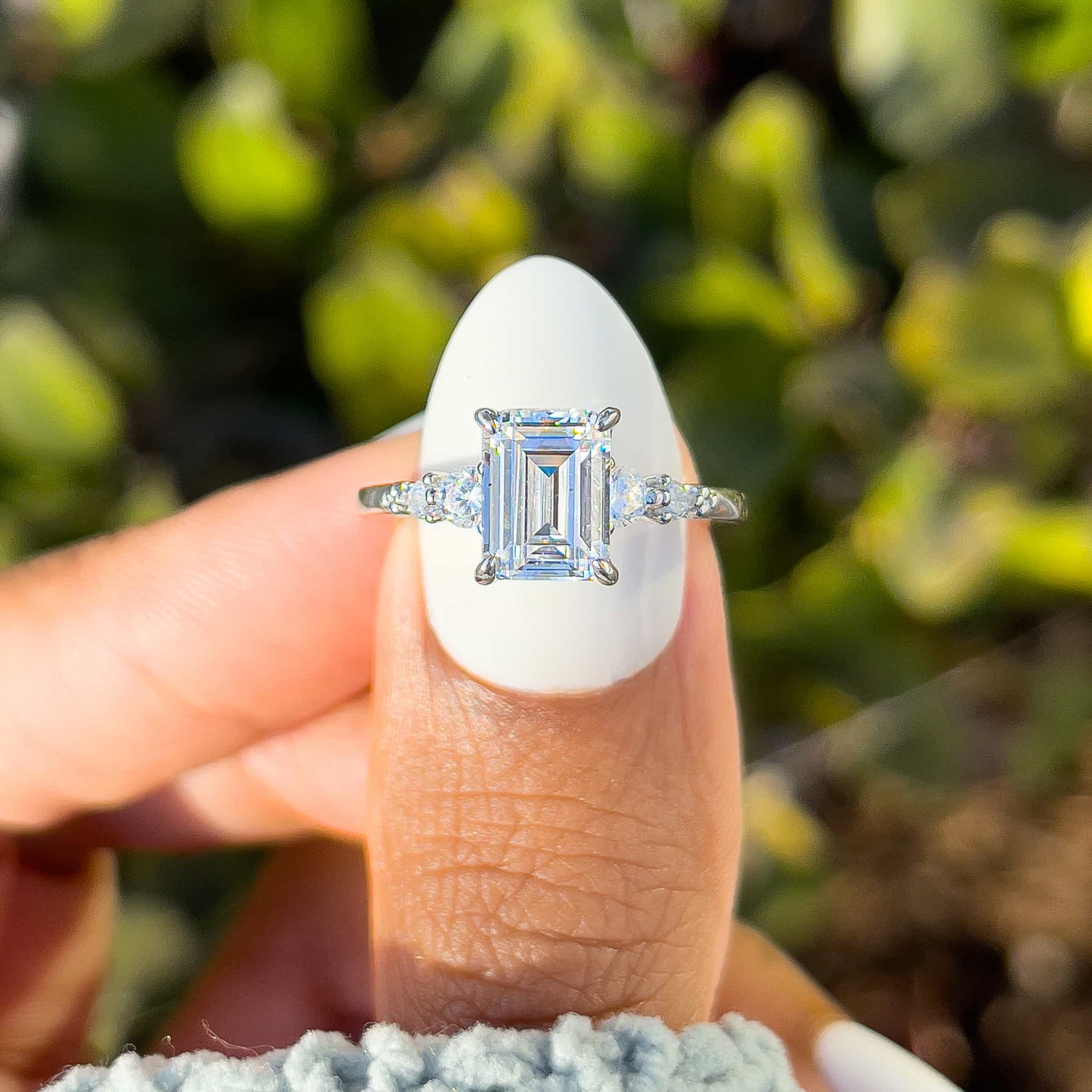 simple silver 1.5 emerald cut engagement ring on model with white nails