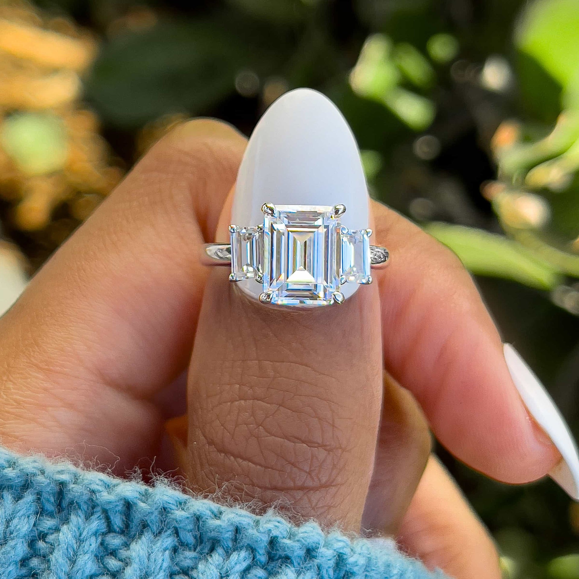 stunning silver emerald cut trio engagement ring on model's hand with blue sweater and white nails