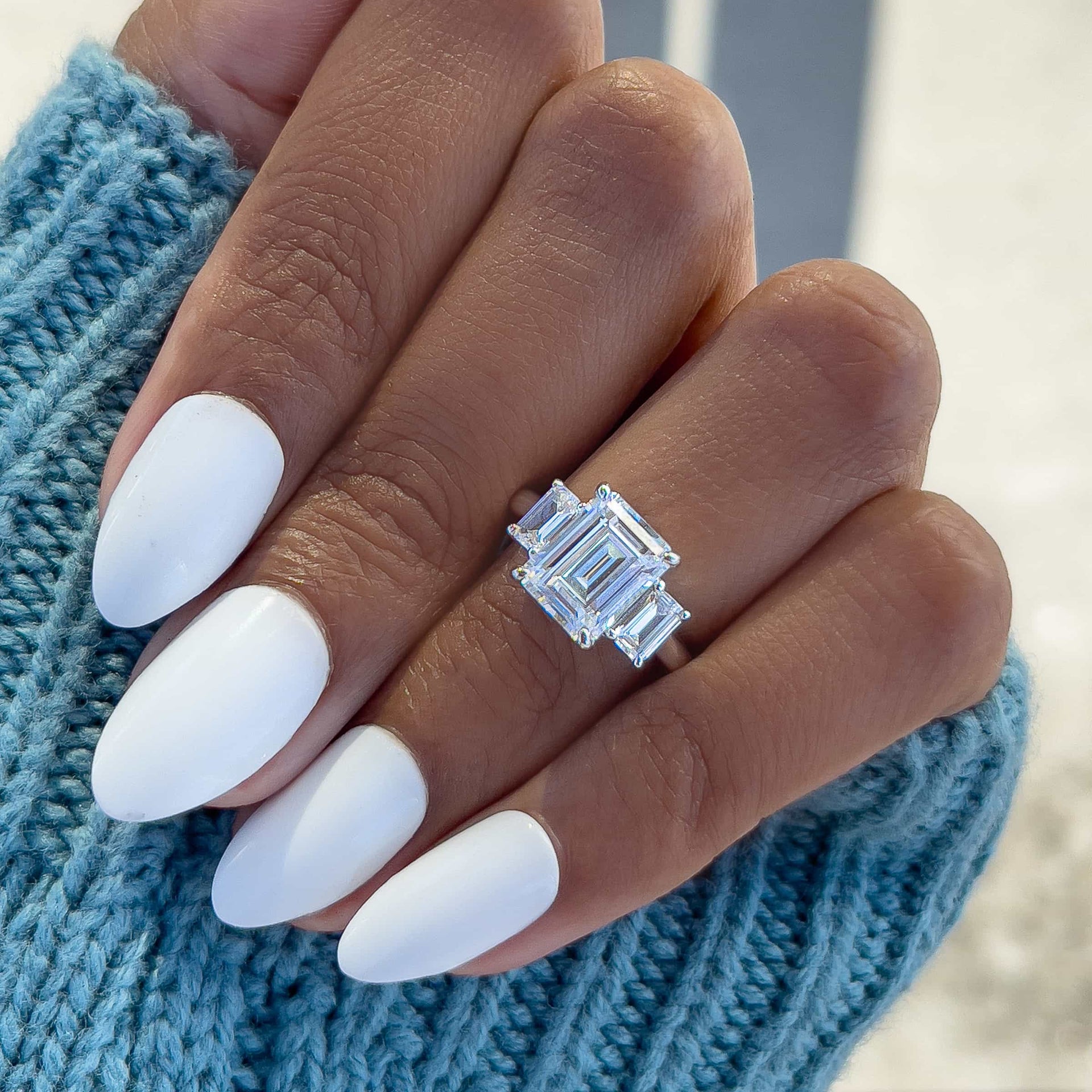 stunning silver emerald cut trio engagement ring on model's hand with blue sweater and white nails