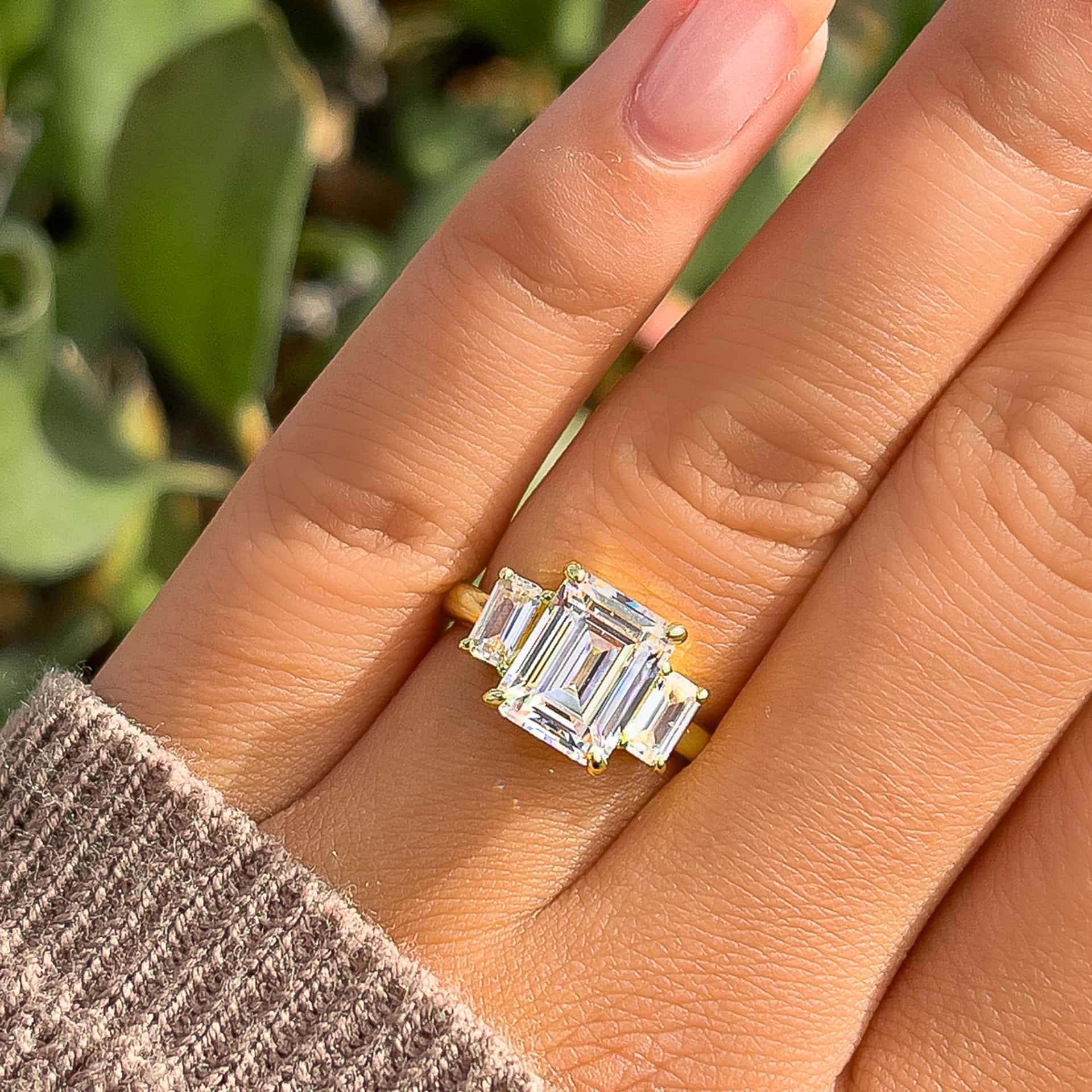 gold boho style trinity emerald cut engagement ring on model with tan sweater