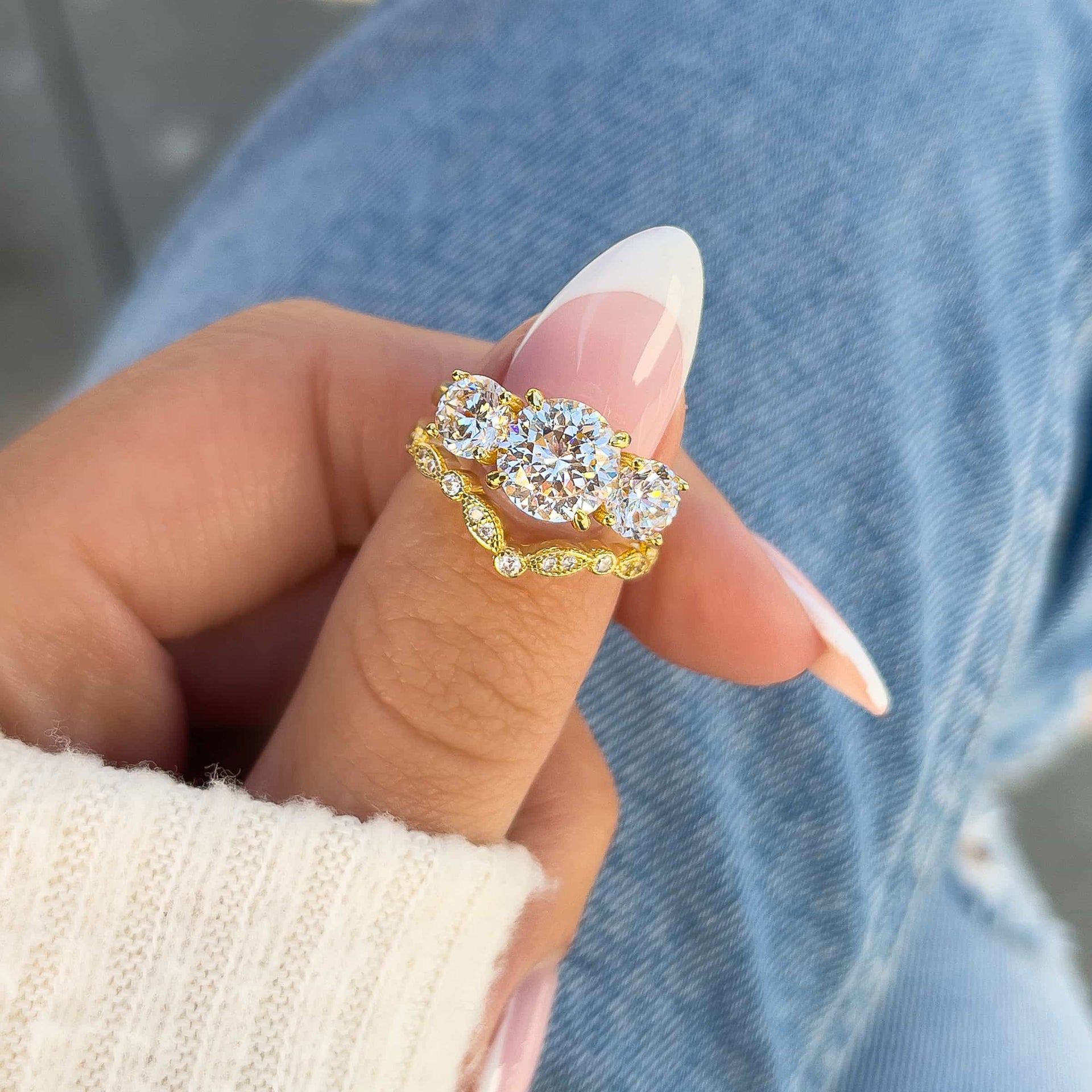 stunning trinity 2ct gold round cut engagement ring paired with chevron wedding band on model's thumb with manicured nails