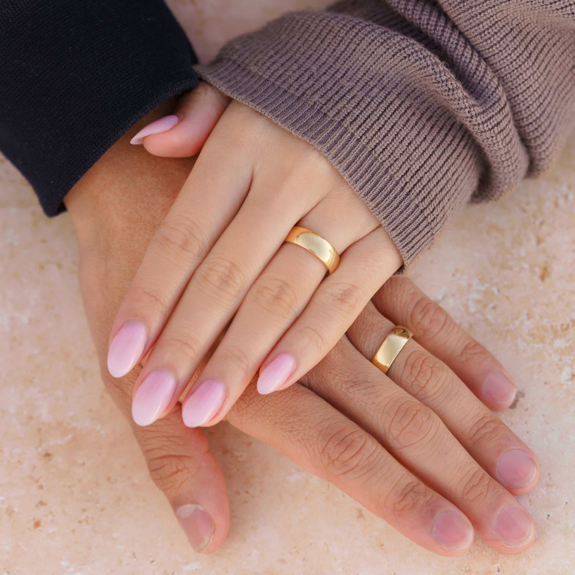 his and hers gold horizon wedding rings on couple's hands with a tan background