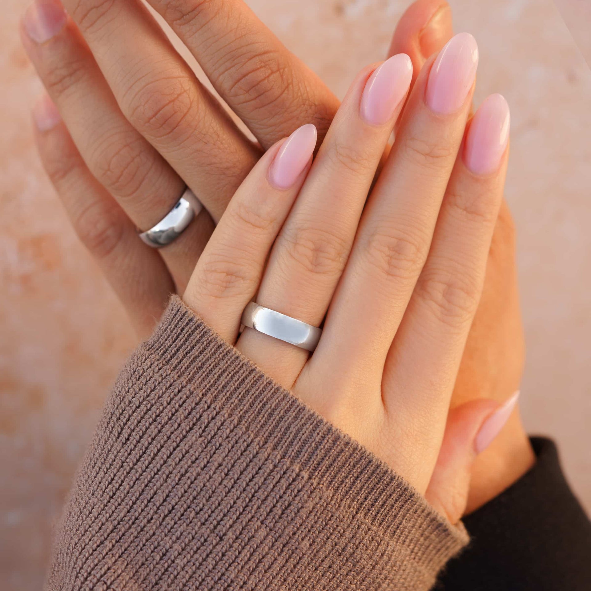 affordable silver unisex Horizon wedding rings showcased on a couple's hands with a tan background