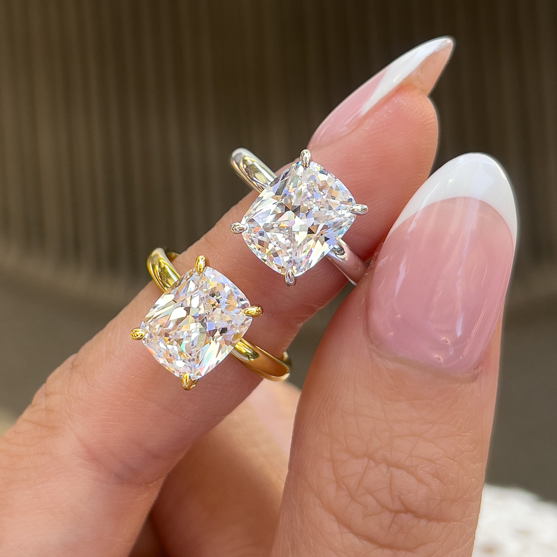a bold 4 carat elongated cushion cut solitaire engagement ring shown in silver and gold on model with french tip nails