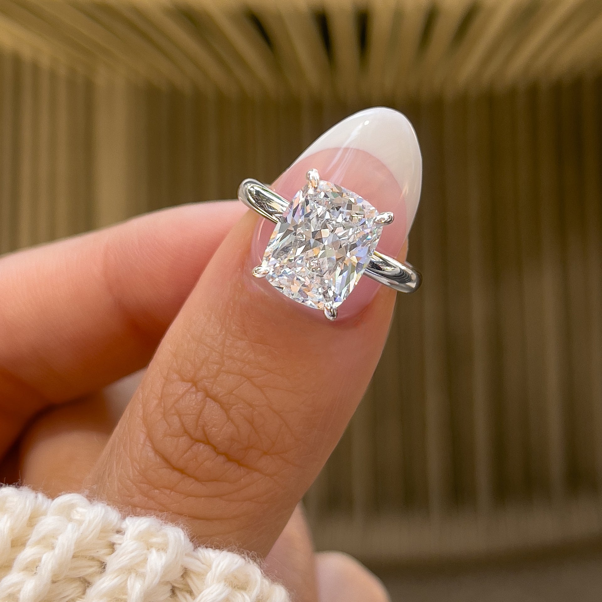Simple silver elongated cushion cut solitaire engagement ring on model with french tips nails and a cream sweater