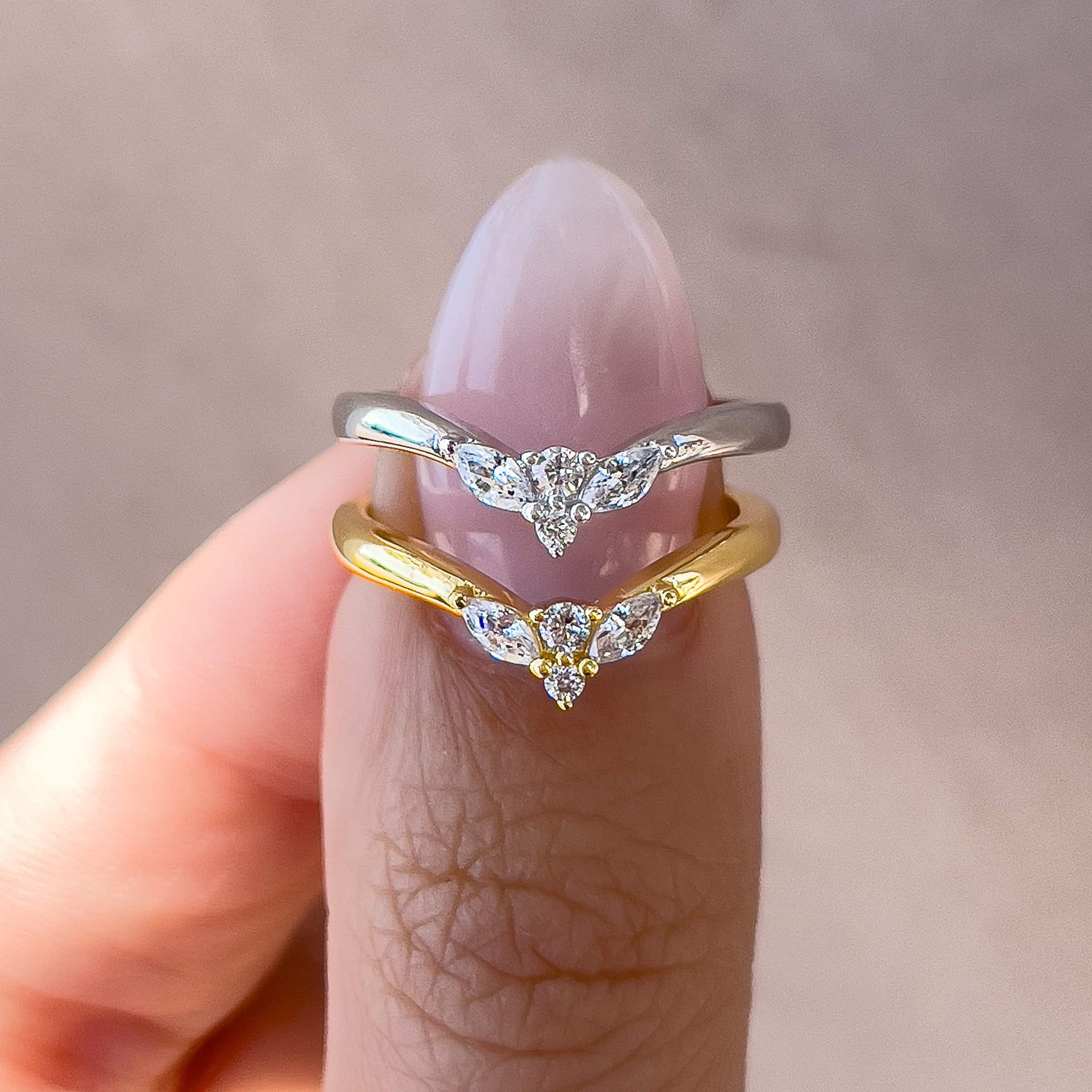 a simple, vintage style chevron wedding band with the daintiest round and marquise cut stone detailing shown in silver and gold on a model with neutral nails