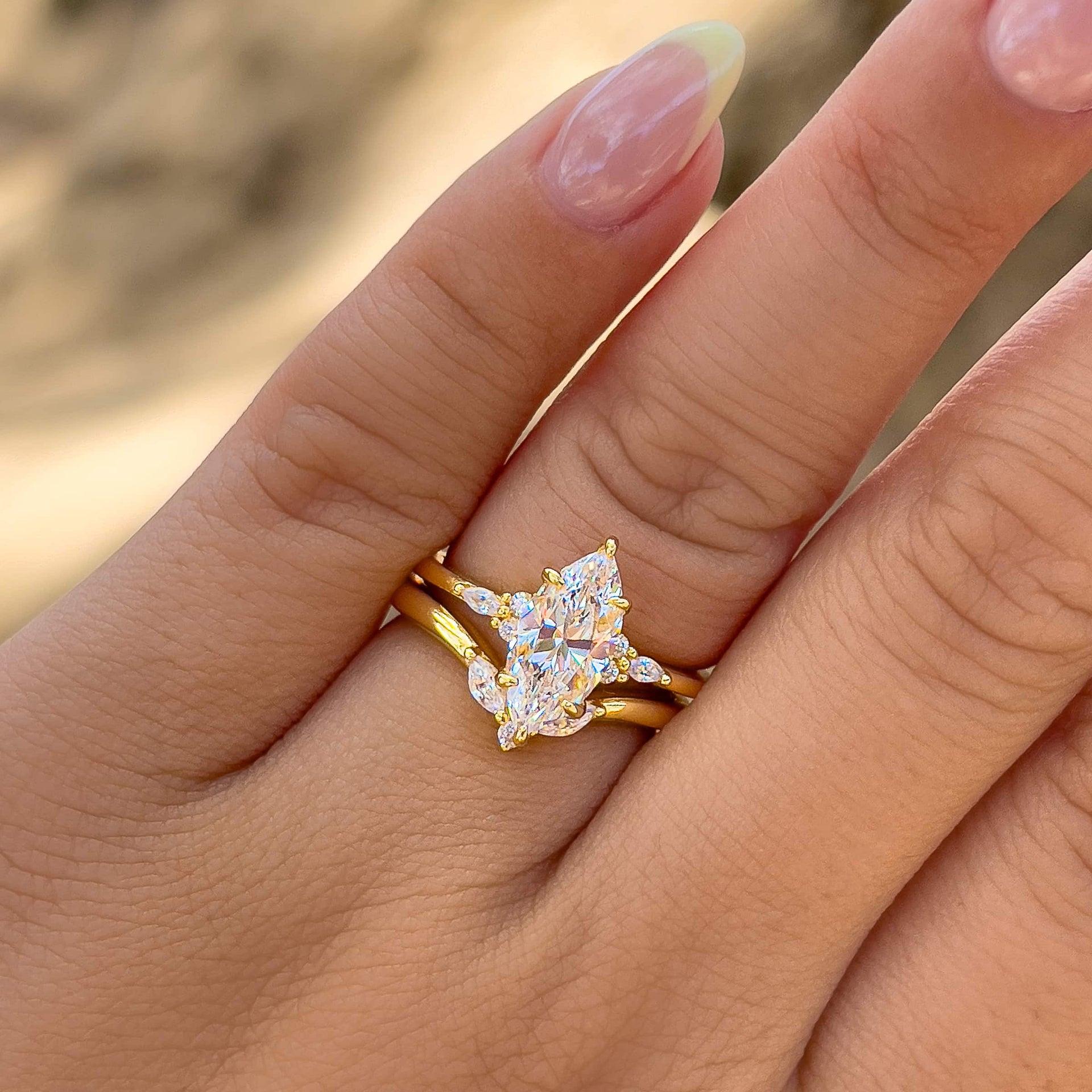 gorgeous gold wedding set made up of a stunning marquise cut engagement ring and simple, vintage chevron wedding band on model with light yellow chrome french tip nails