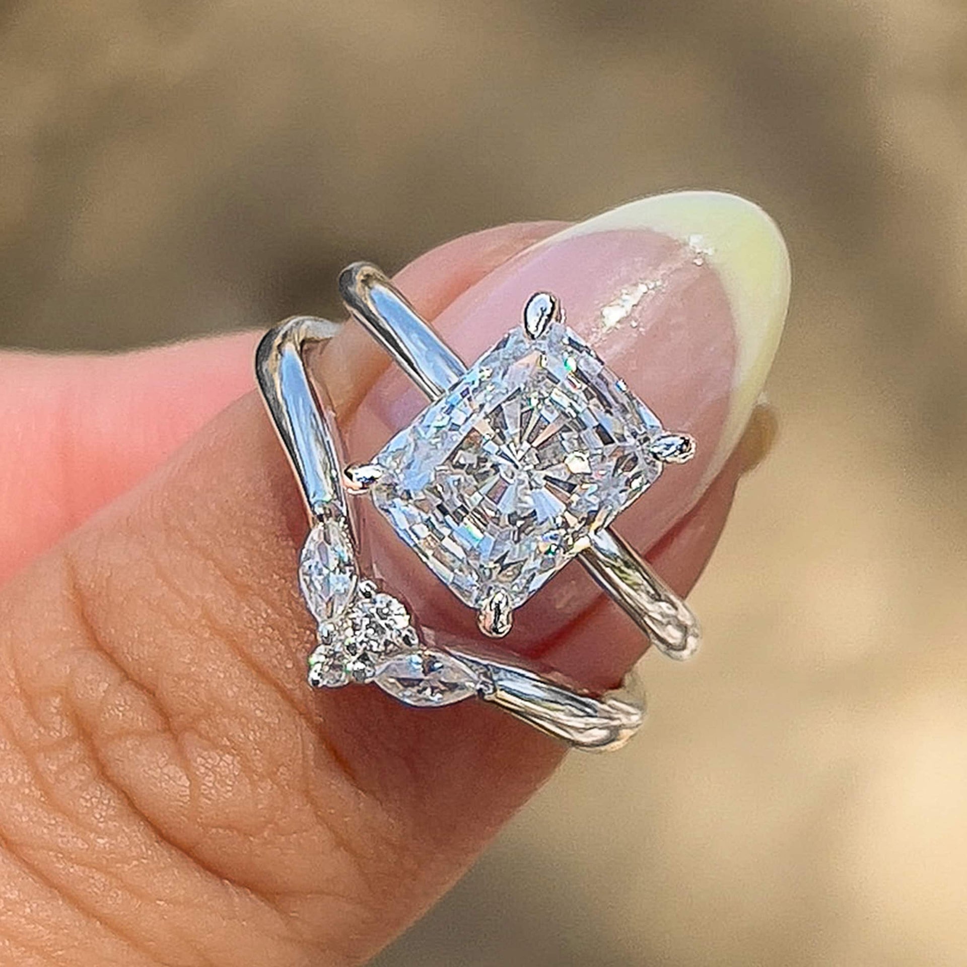 silver wedding set with radiant cut solitaire ring and vintage chevron wedding band held by model with light yellow chrome french tip nails