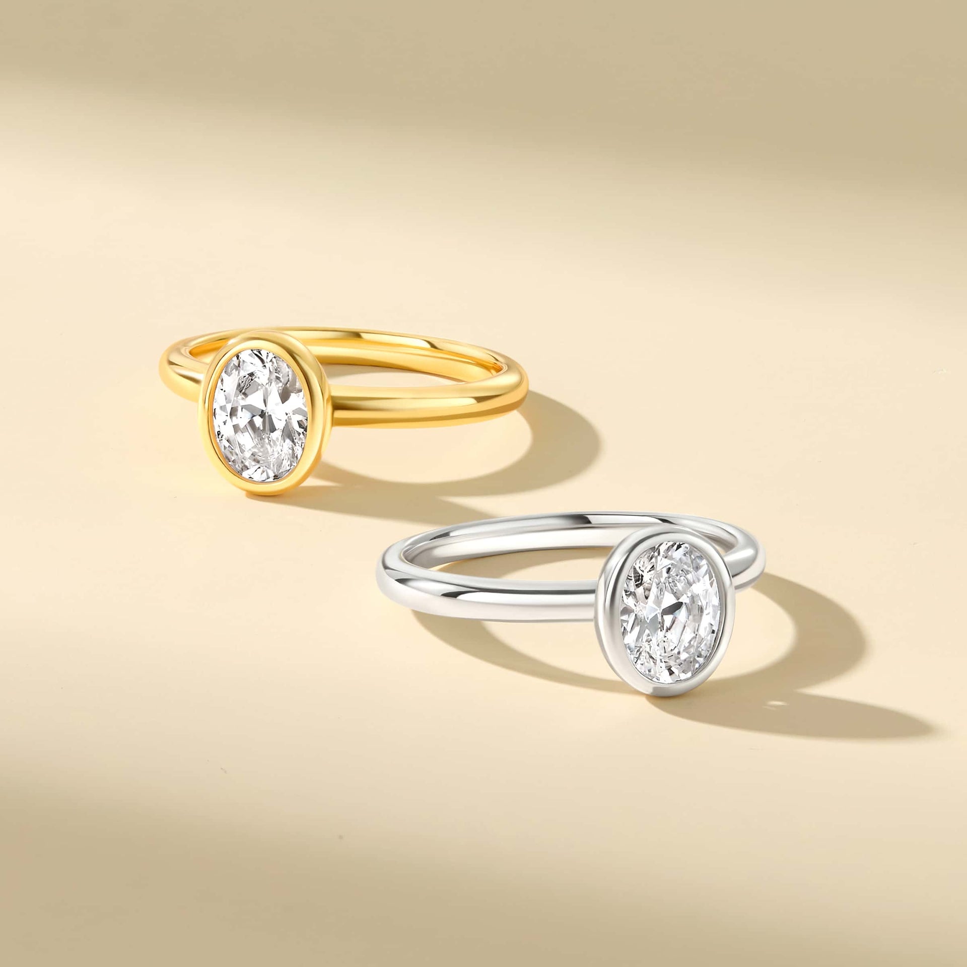 flay lay image of two oval-cut bezel rings in silver and gold on a tan background