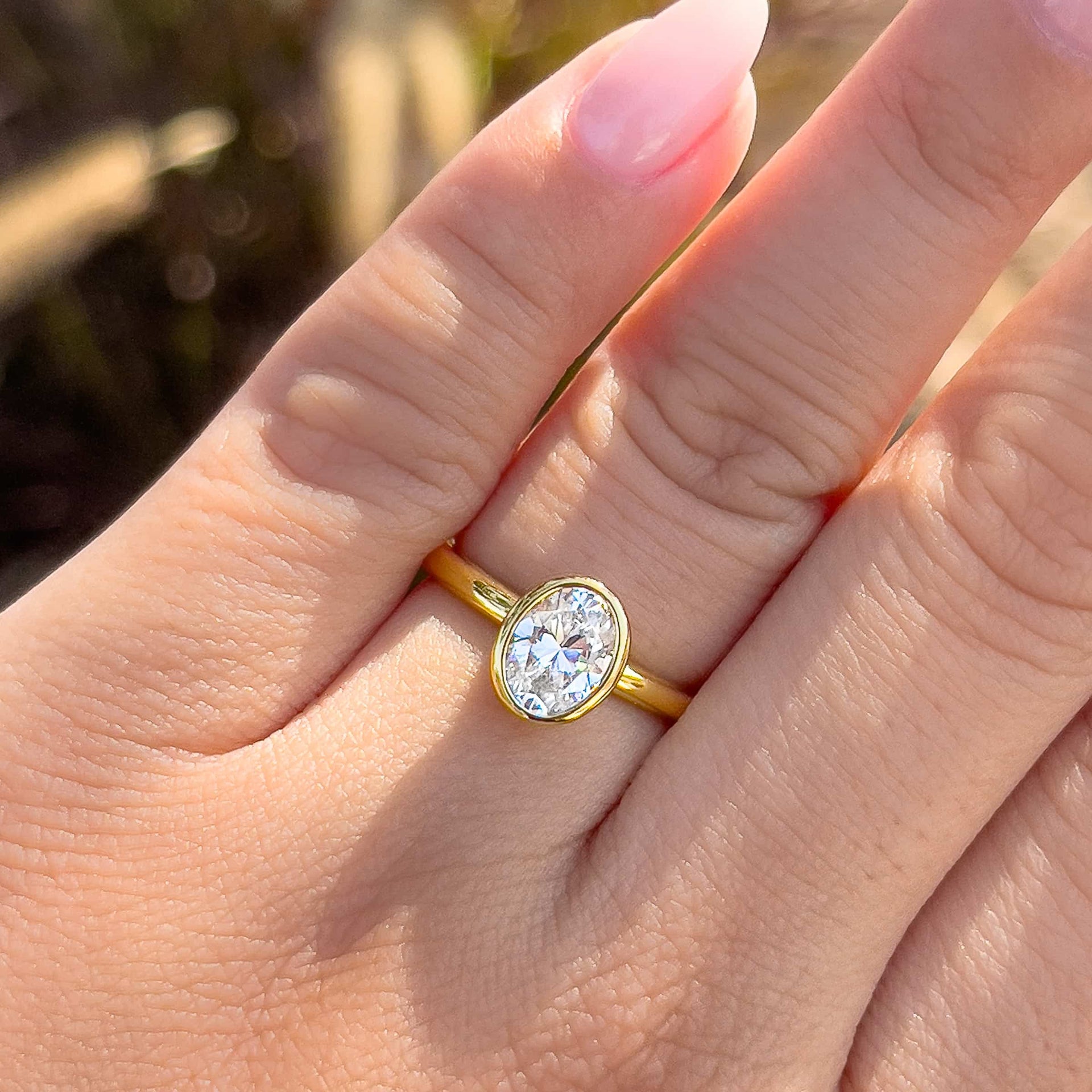 a beautiful oval cut gold engagement ring shown alone on model's ring finger with pink manicured nails