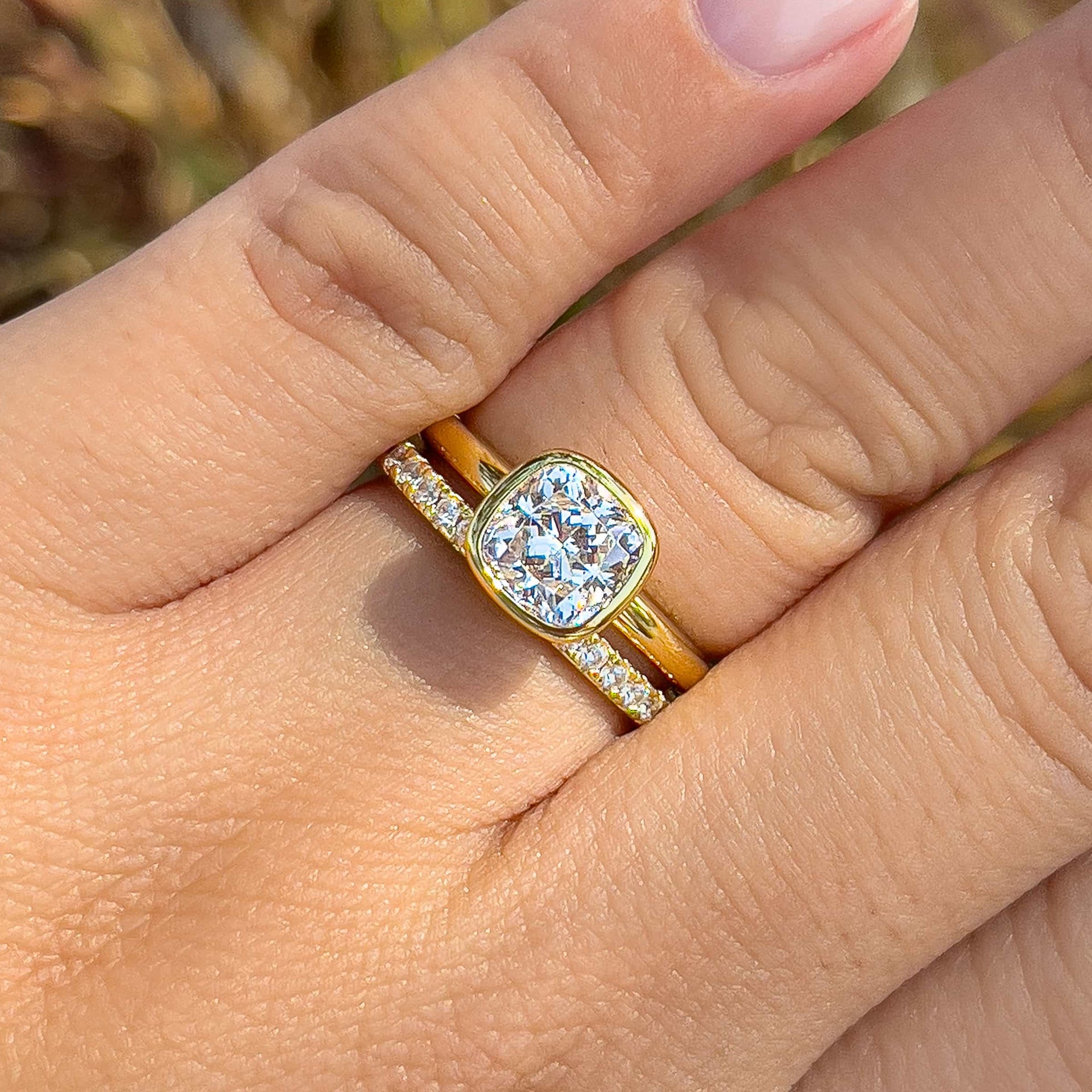 a beautiful cushion cut bezel engagement ring in gold on model's ring finger with an eternity wedding band 