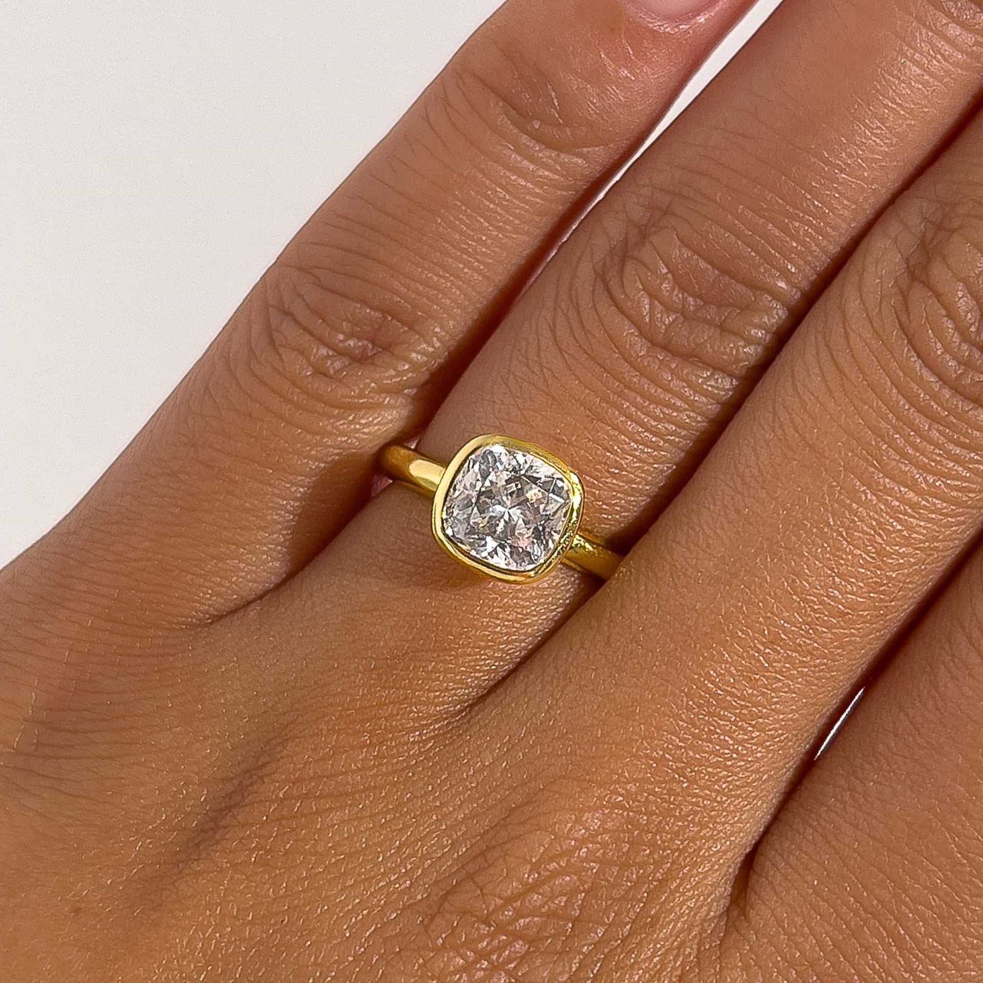a stunning gold bezel engagement ring with a cushion cut center stone on model's ring finger 
