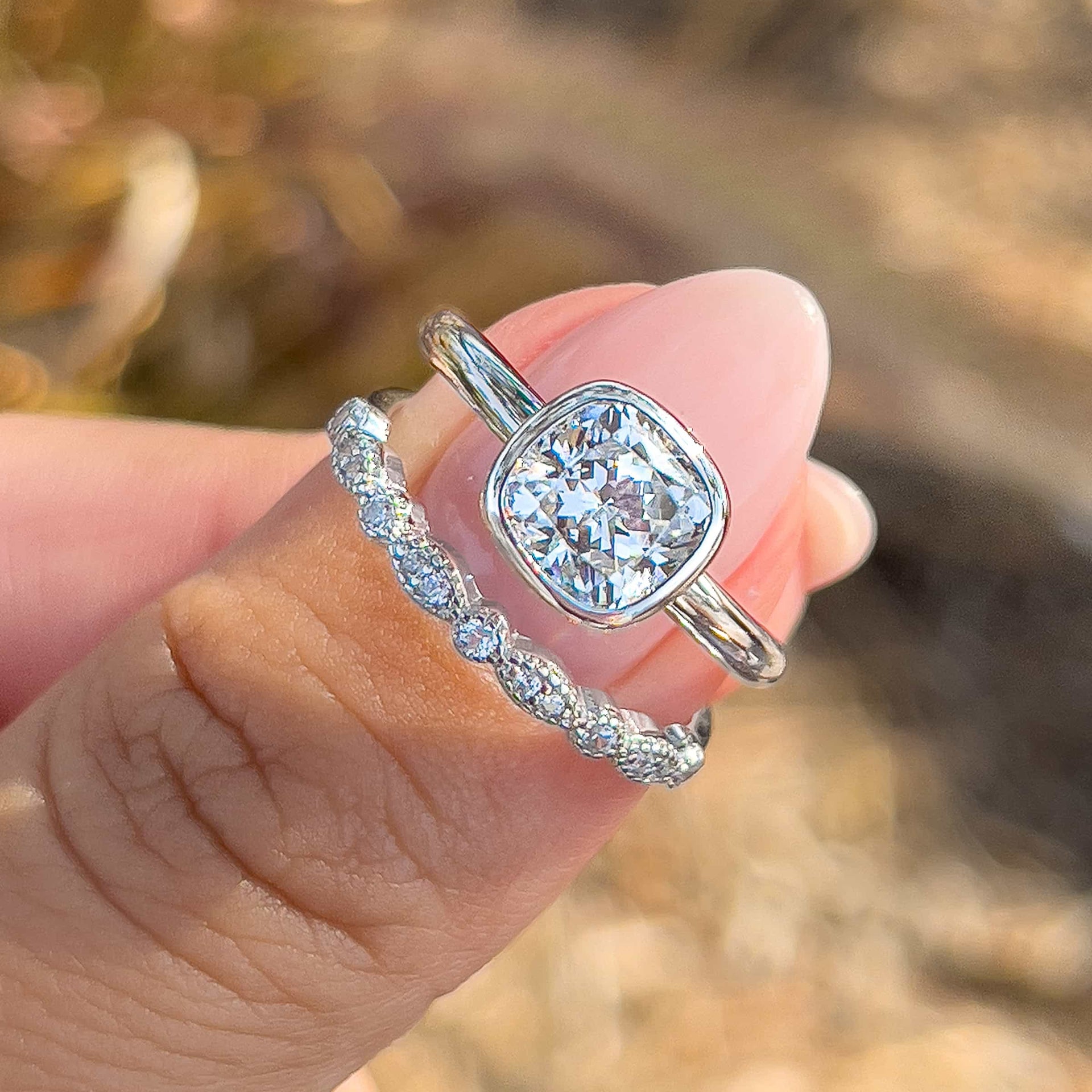 a stunning silver bezel engagement ring with a cushion cut center stone and a pave silver wedding band on model's thumb 