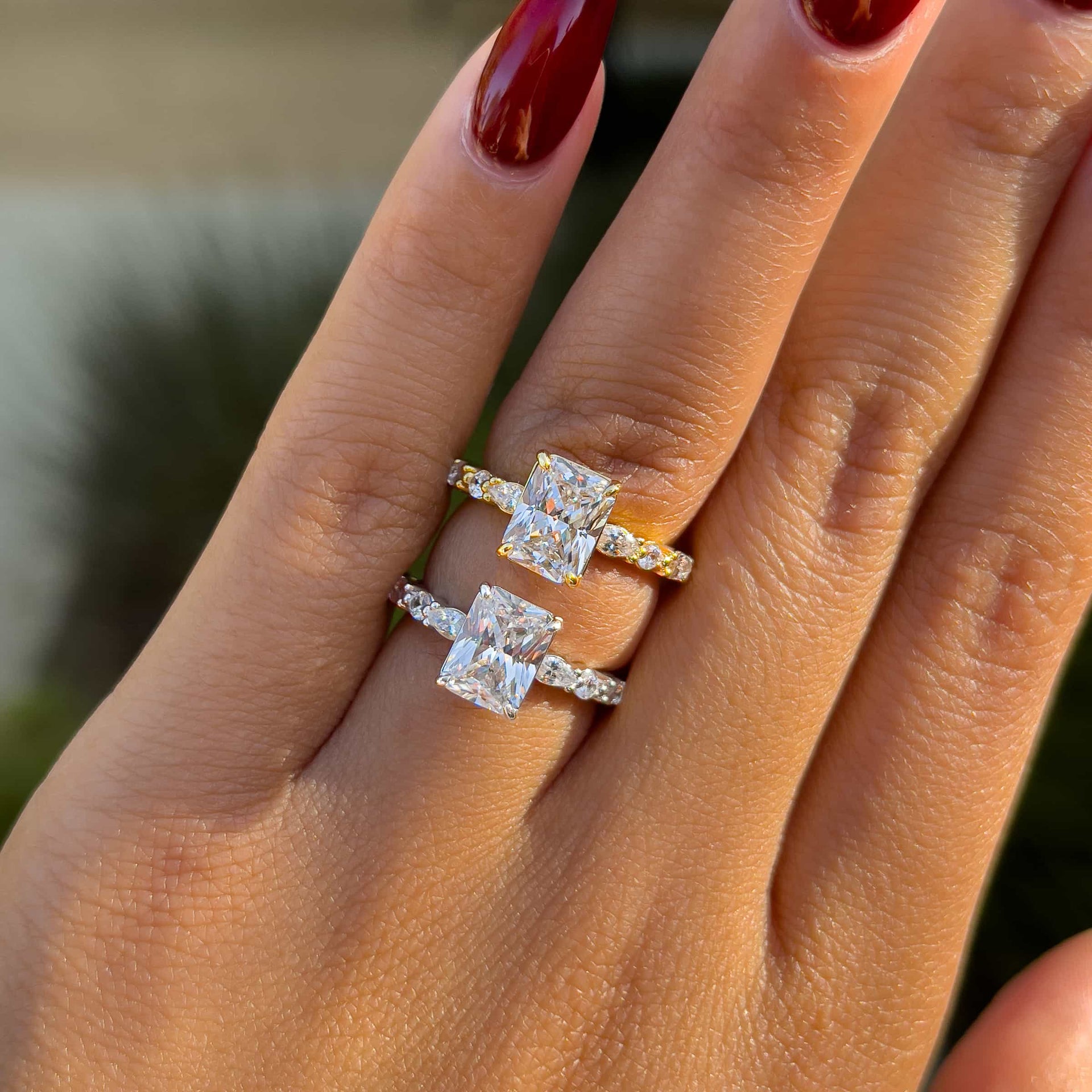 2 carat half eternity radiant cut engagement ring shown in gold and silver on a model with deep red nails