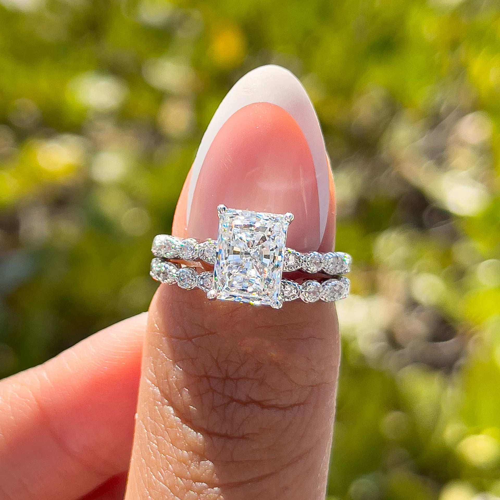 sparkling silver vintage 1.5 carat radiant cut half eternity wedding ring set on model with french tip nails in front of greenery