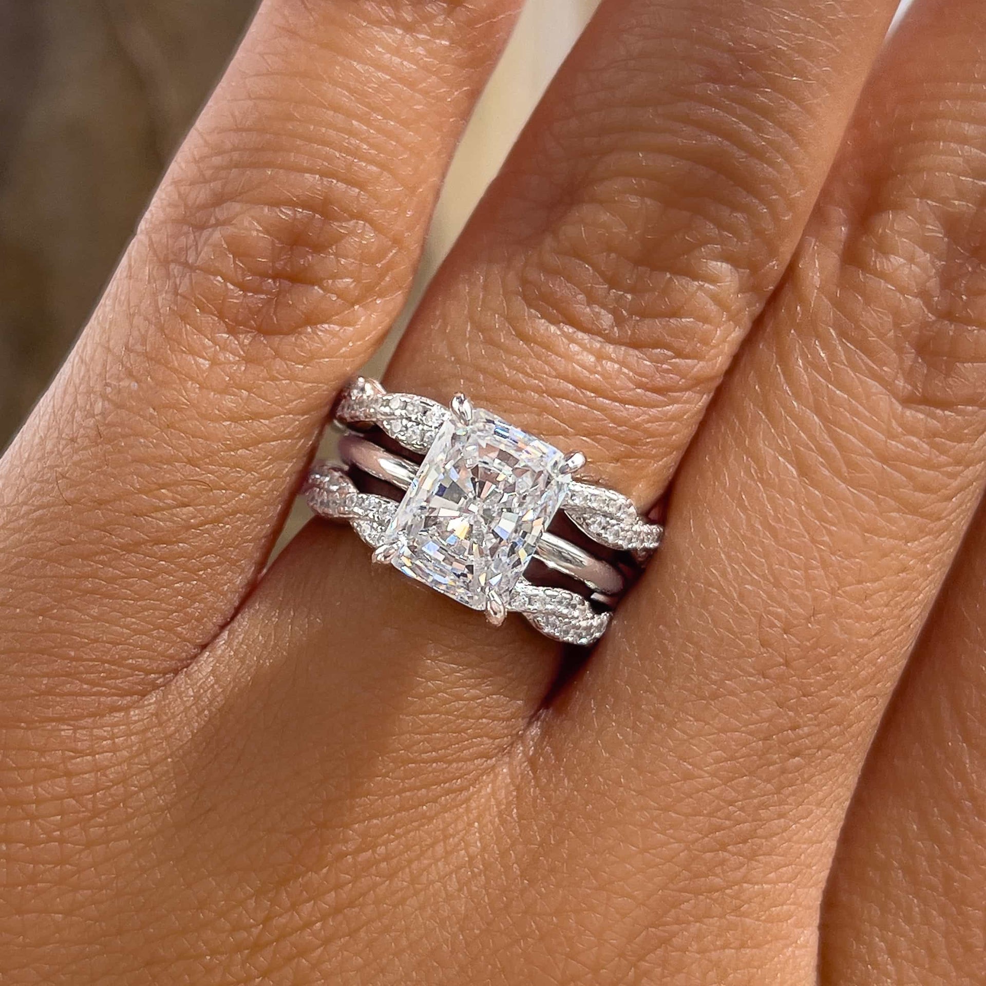 silver radiant cut wedding ring set paired with a 2nd full twisted eternity band to create a triple ring stack worn by female model