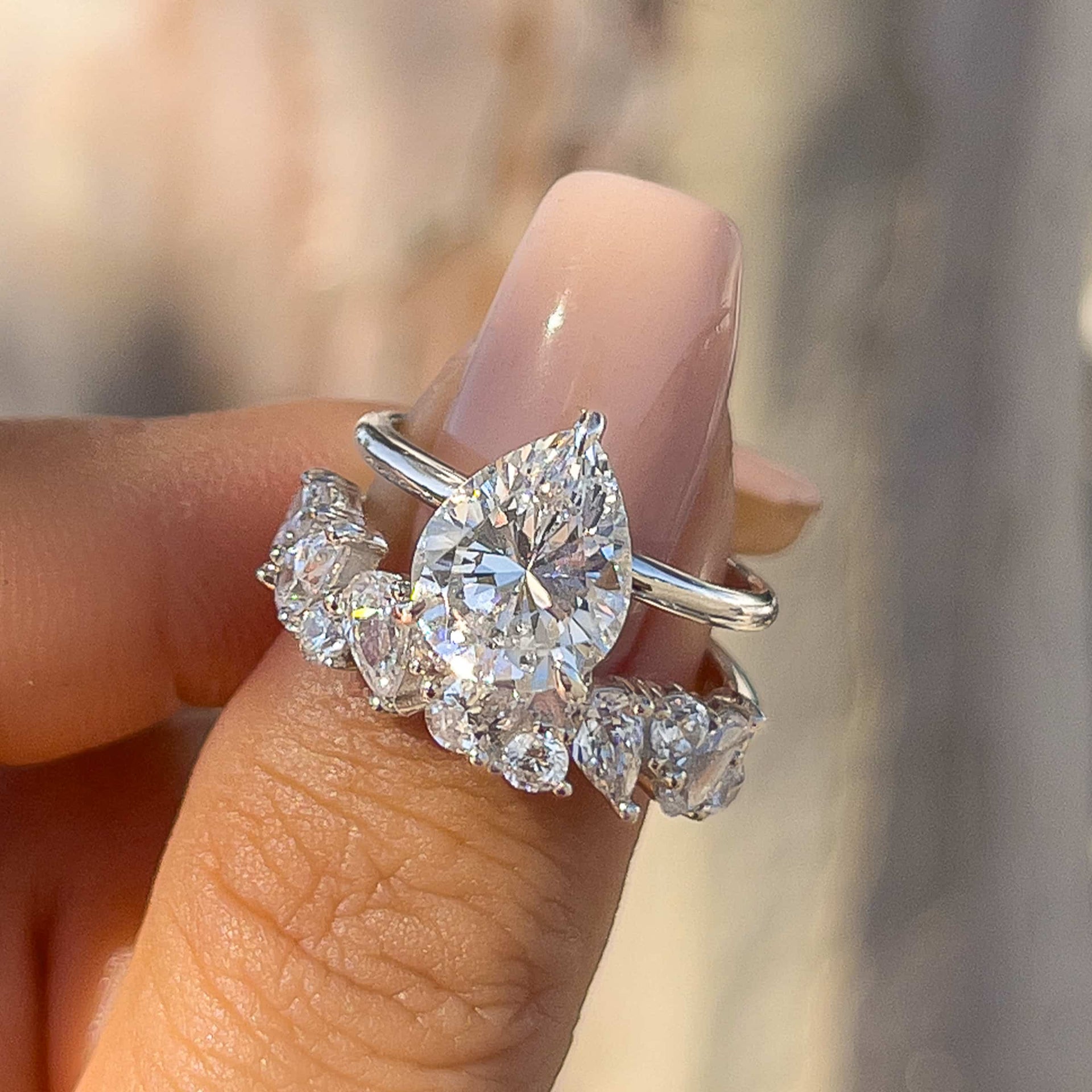 bold 3 carat pear cut wedding ring set held by model with light pink nails