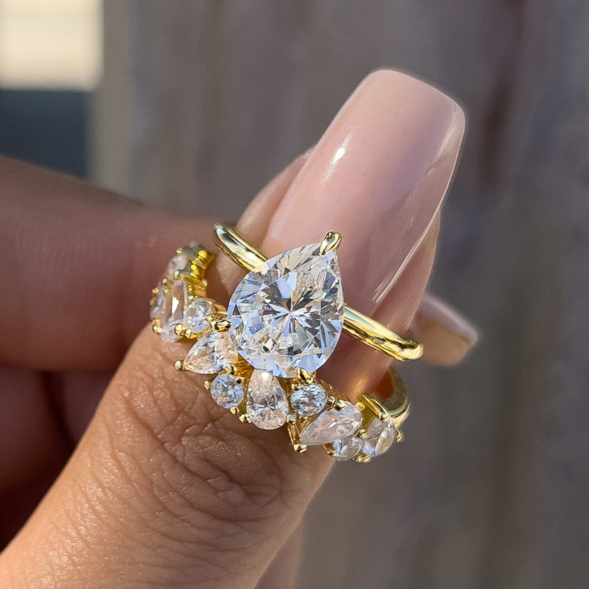 bold 3 carat pear cut wedding ring set held by model with light pink nails