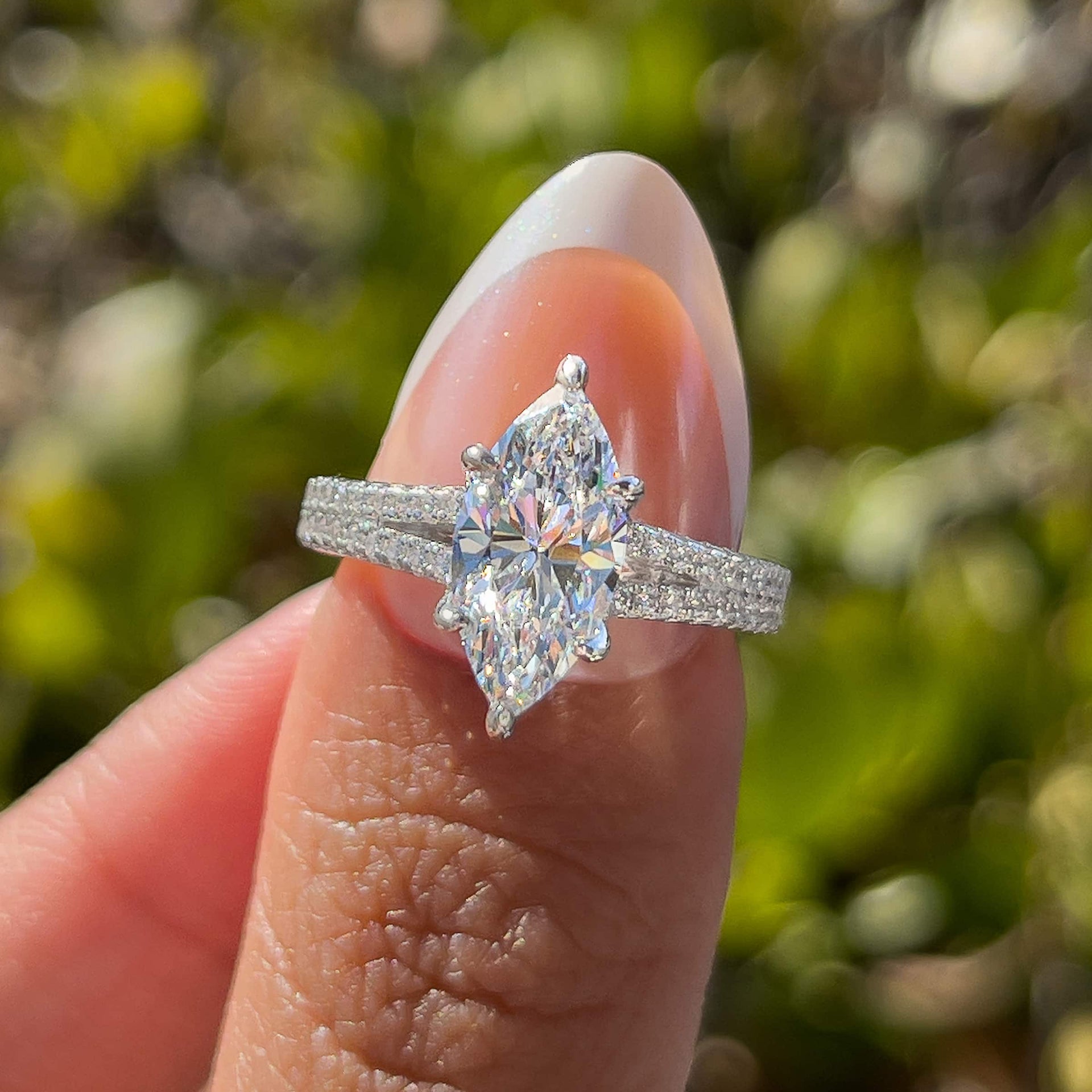 2 carat marquise cut split shank half eternity engagement ring in silver held by model with french tip nails