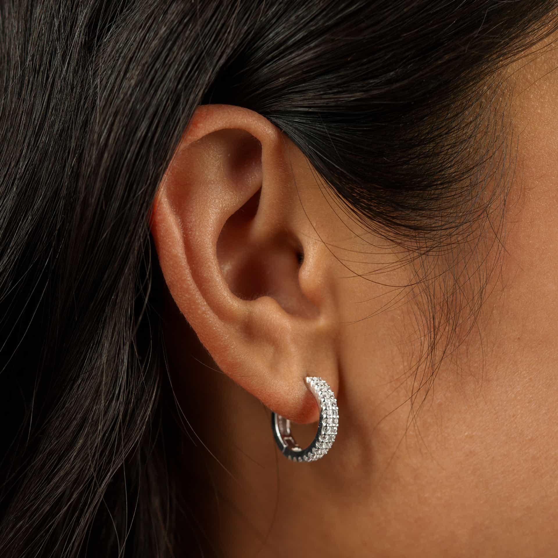 a pair of silver hoops with a double row of stones on a white background worn by model with dark hair