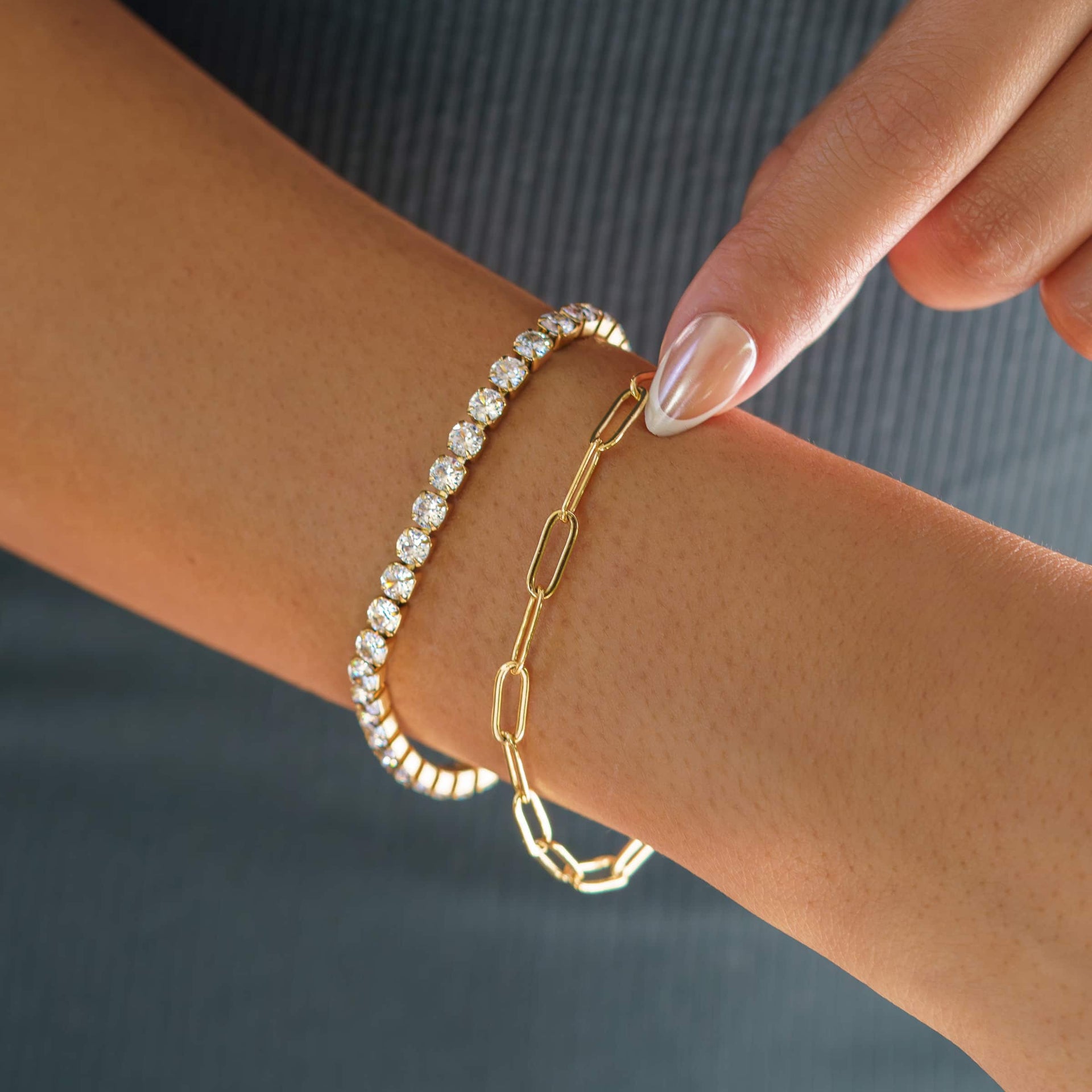 everyday gold tennis bracelet worn as a part of a bracelet stack with a gold paperclip necklace by model with chrome and french tip nails
