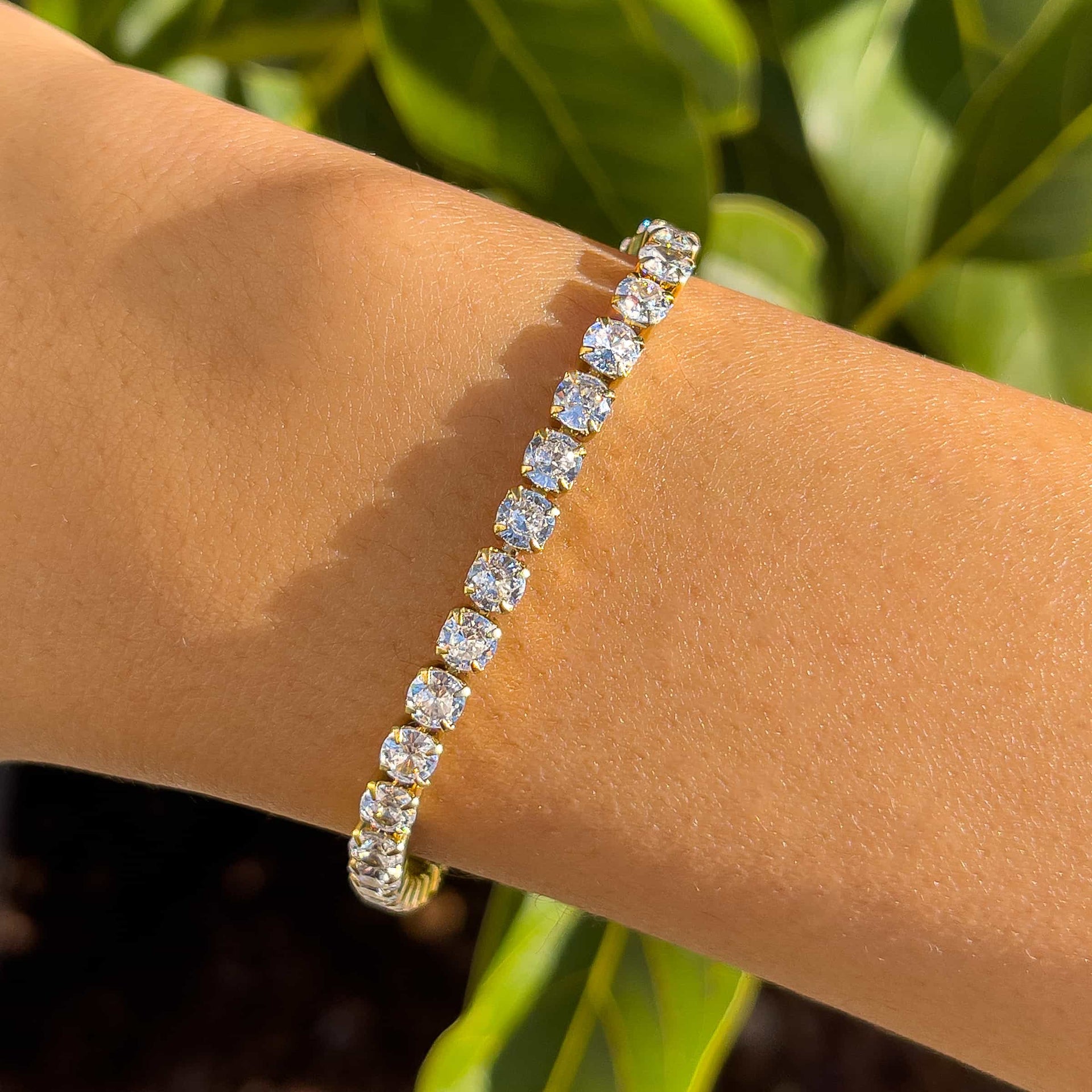 close up shot of a gold stainless steel tennis bracelet on model in front of greenery