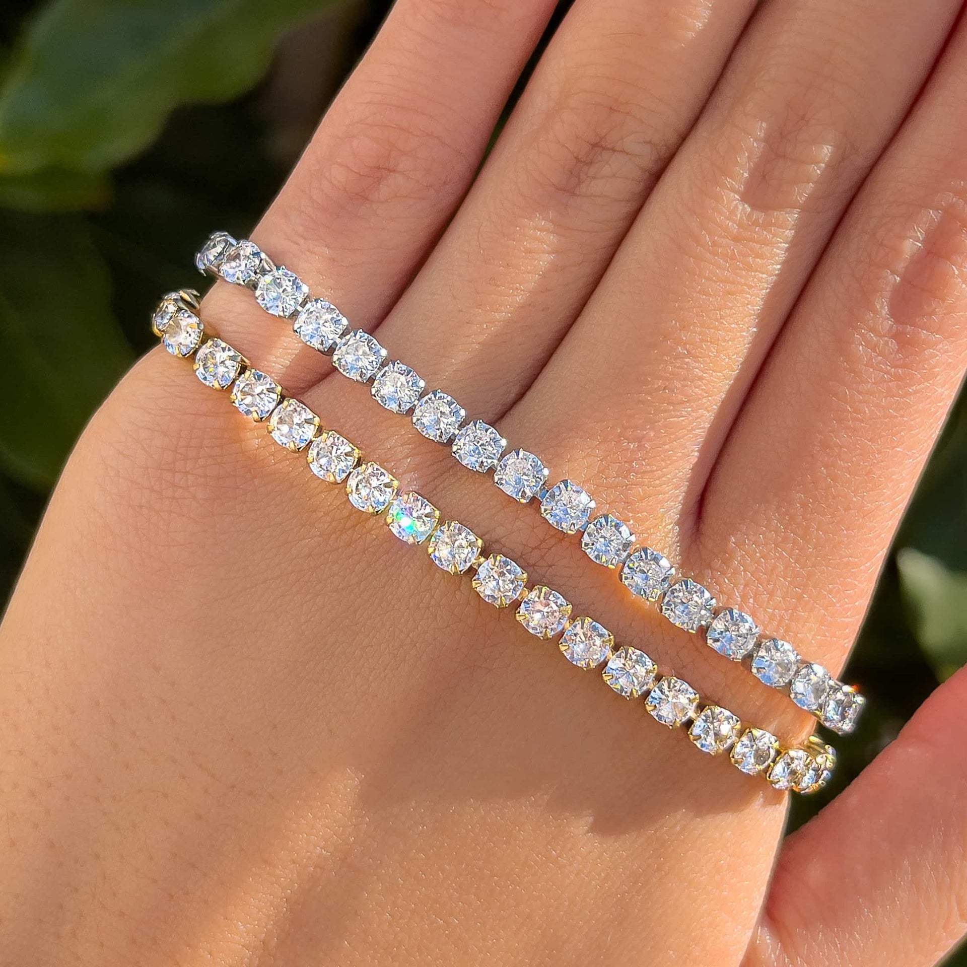 a sparkling tennis bracelet shown in both silver and gold on a model in front of greenery