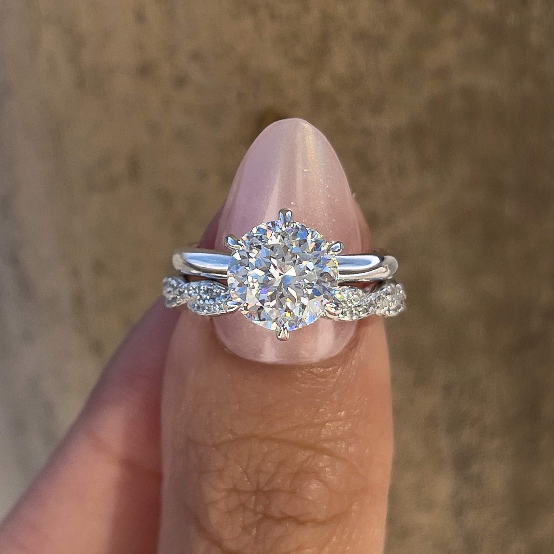 Silver wedding ring set made up of a 2 carat round cut solitaire engagement ring and twisting pave eternity wedding band, held together by a model with light pink nails