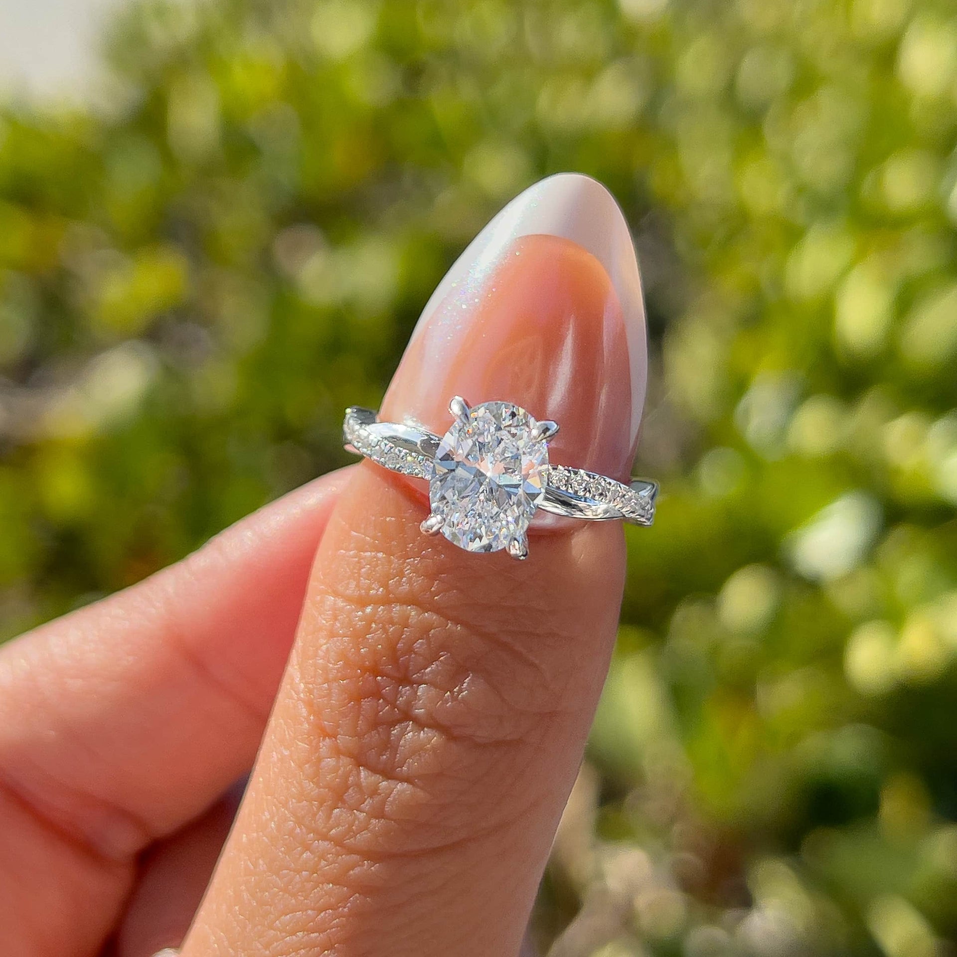 stunning silver vintage 1.5 carat oval cut twisting detail engagement ring held by model with french tip nails in front of greenery