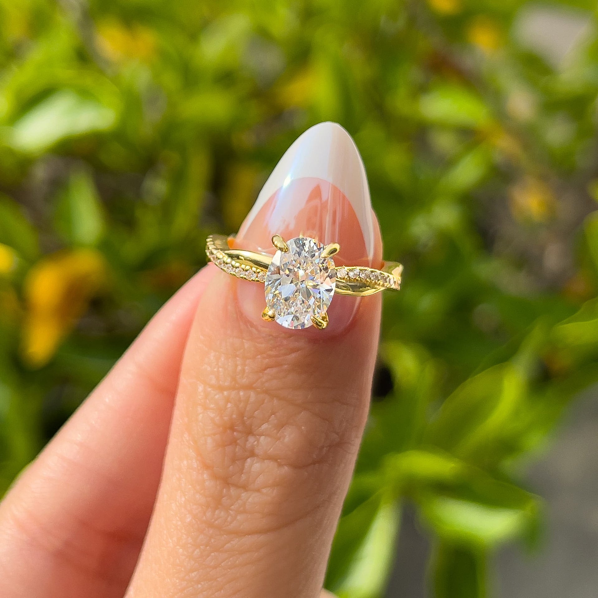 stunning gold vintage 1.5 carat oval cut twisting detail engagement ring held by model with french tip nails in front of greenery
