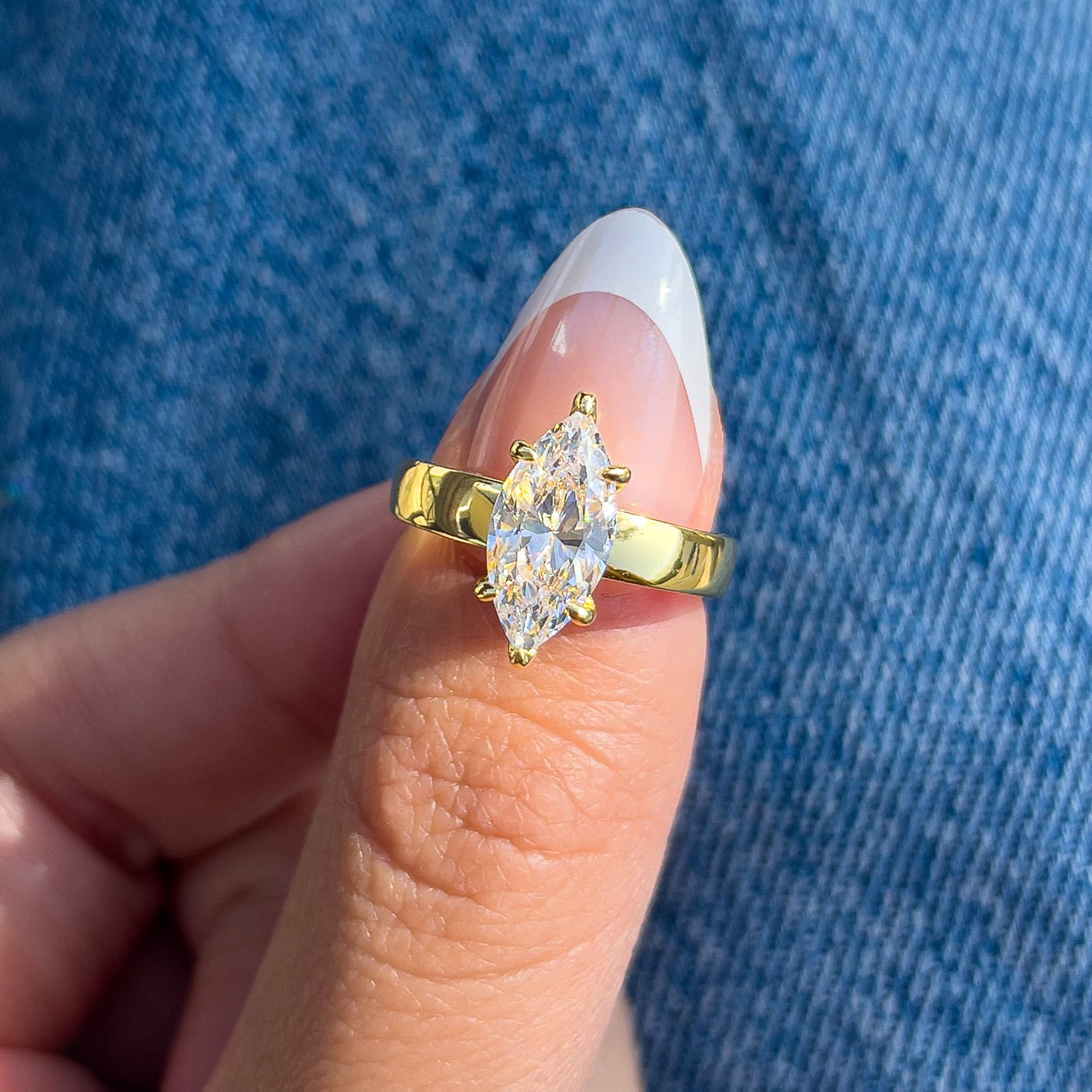 thick gold 2 carat marquise cut solitaire engagement ring on model with french tip nails wearing denim