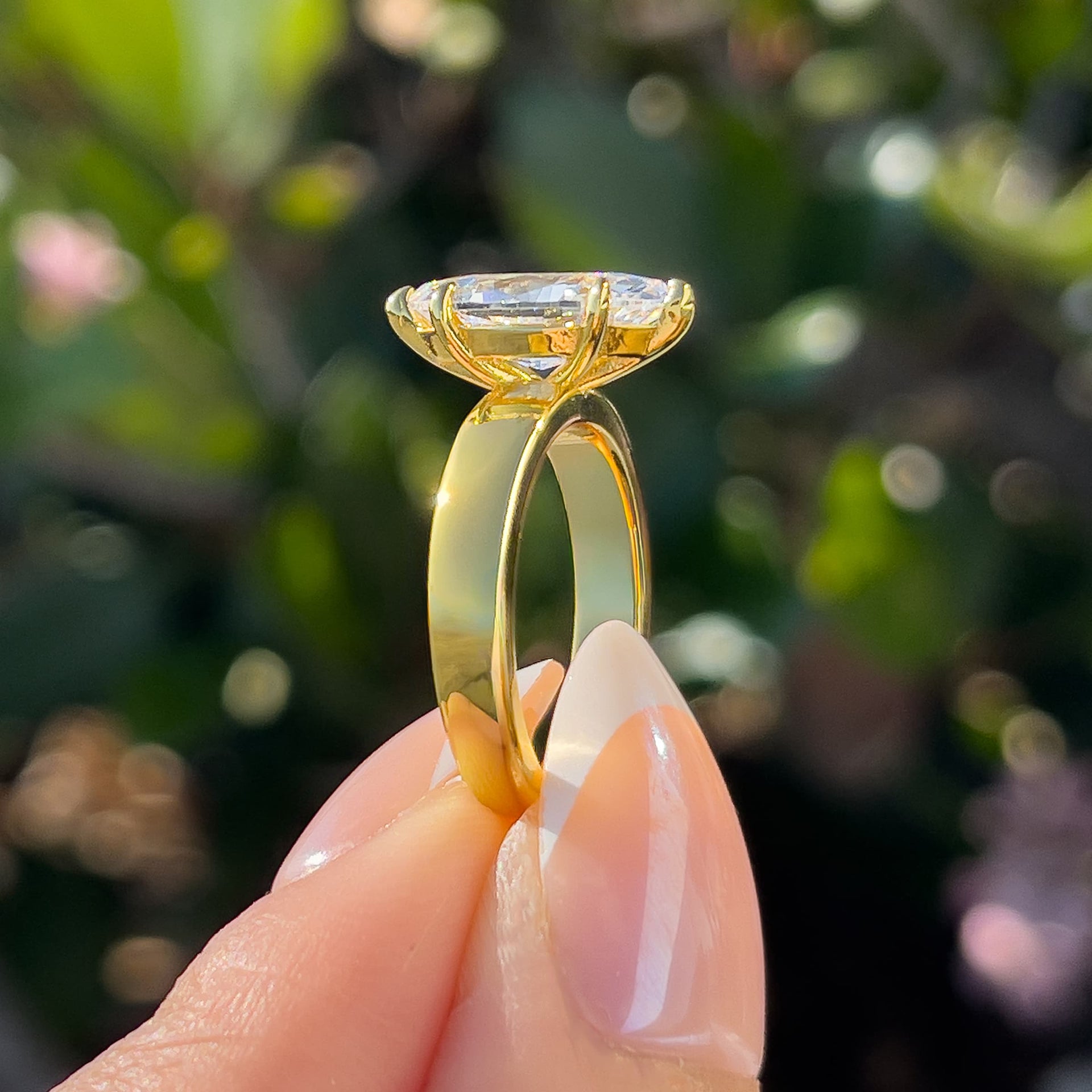 side view of gold 2 carat marquise cut solitaire held by model with french tip nails in front of greenery