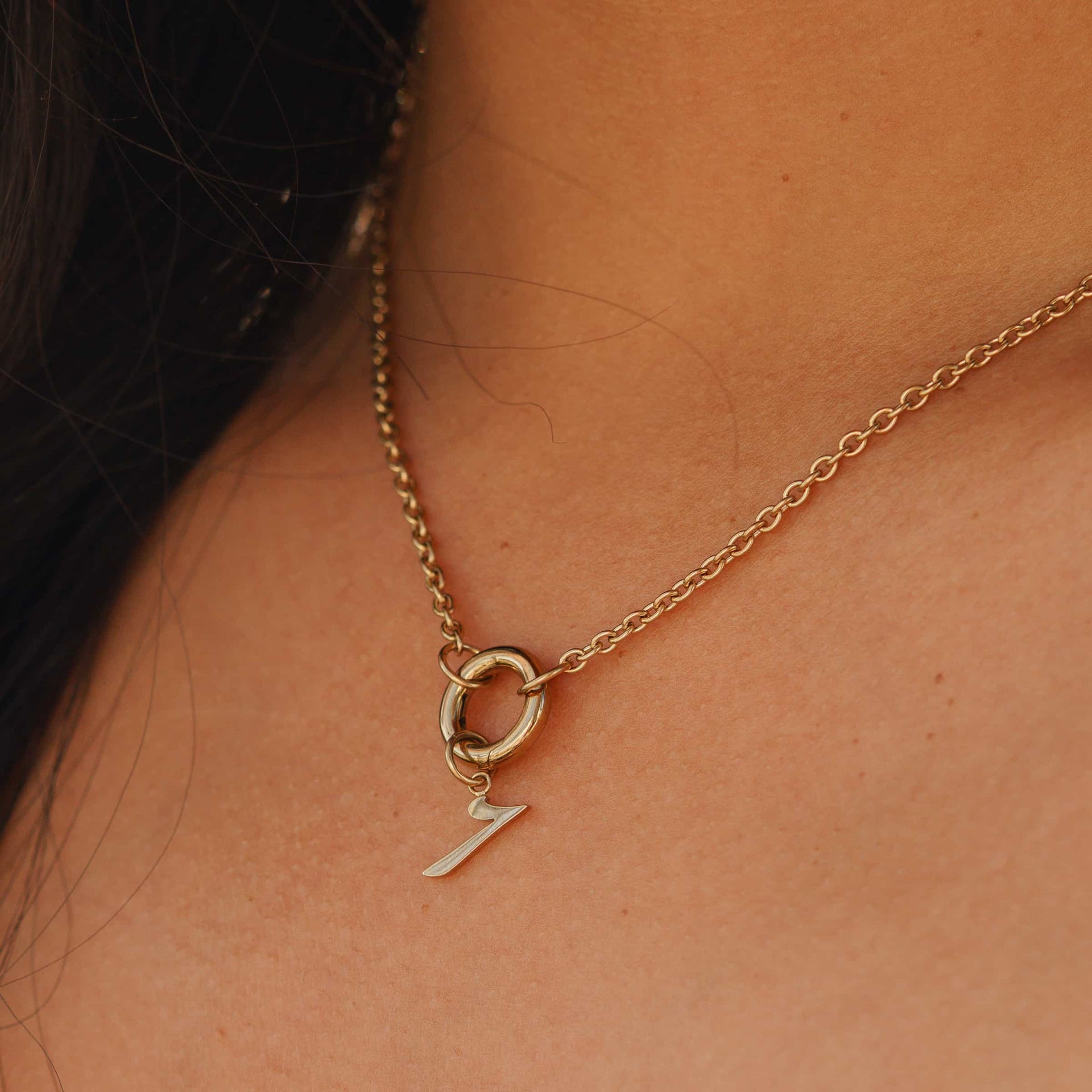 stainless steel number charm "7" shown on a gold stainless steel charm necklace worn by a model with long, dark hair