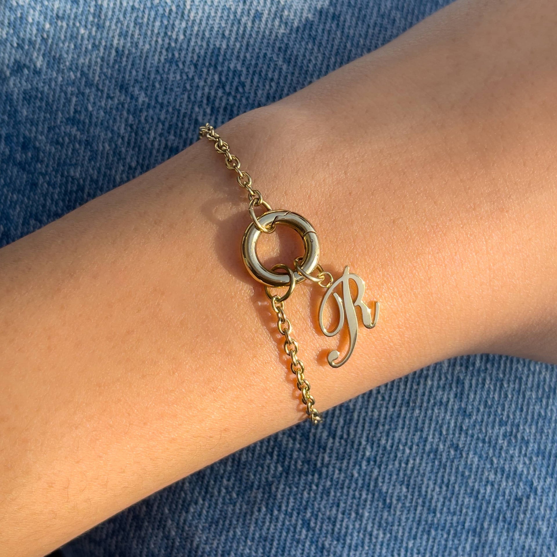 minimalist gold charm bracelet with an "R" initial pendant on a model wearing denim