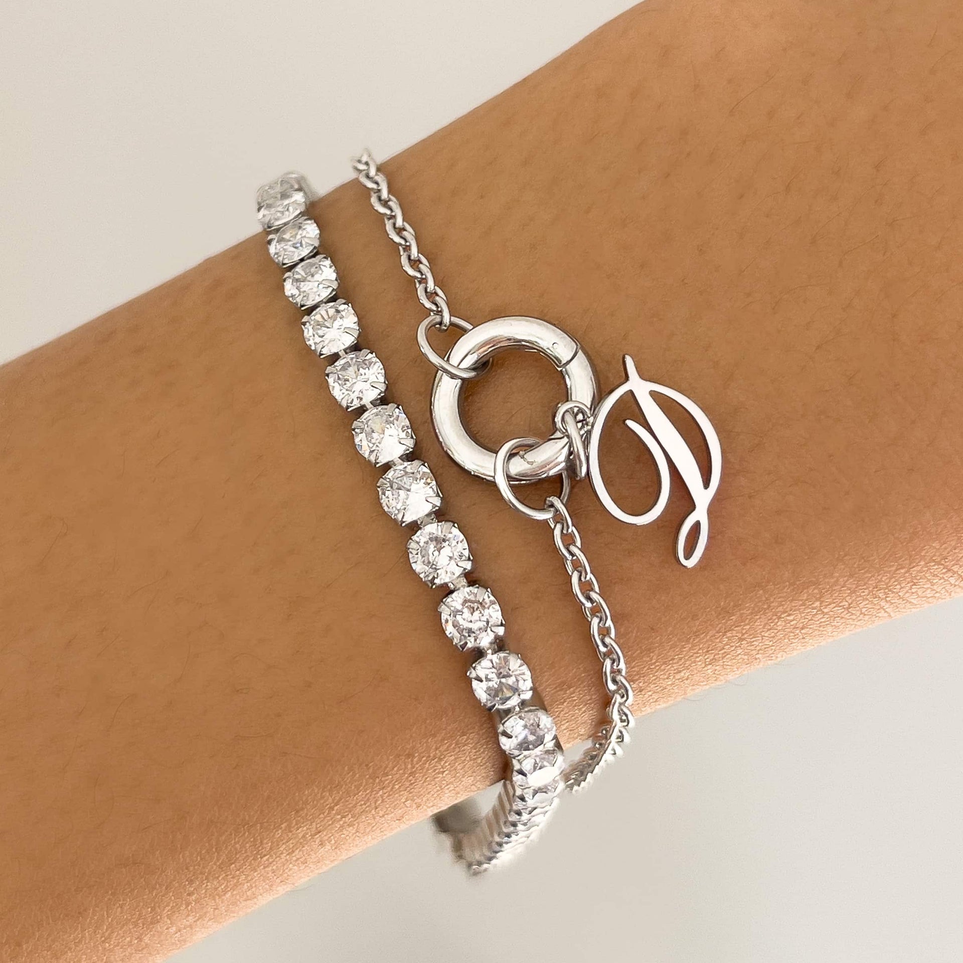 silver stainless steel charm bracelet worn  with the letter charm "D" and stacked with a stainless steel tennis bracelet on a model