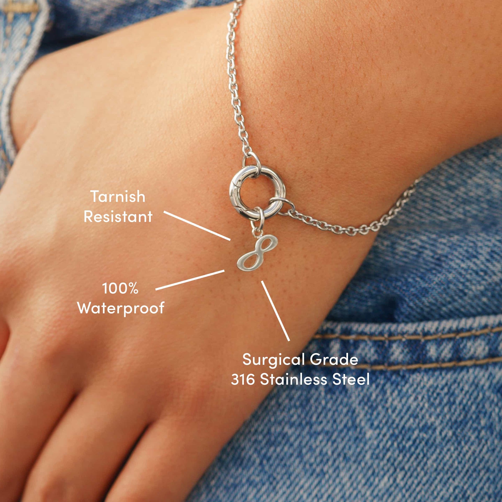 minimalist silver charm bracelet with an "8" number pendant on a model wearing denim with the following text: "Tarnish Resistant", "100% Waterproof", "Surgical Grade 316 Stainless Steel"