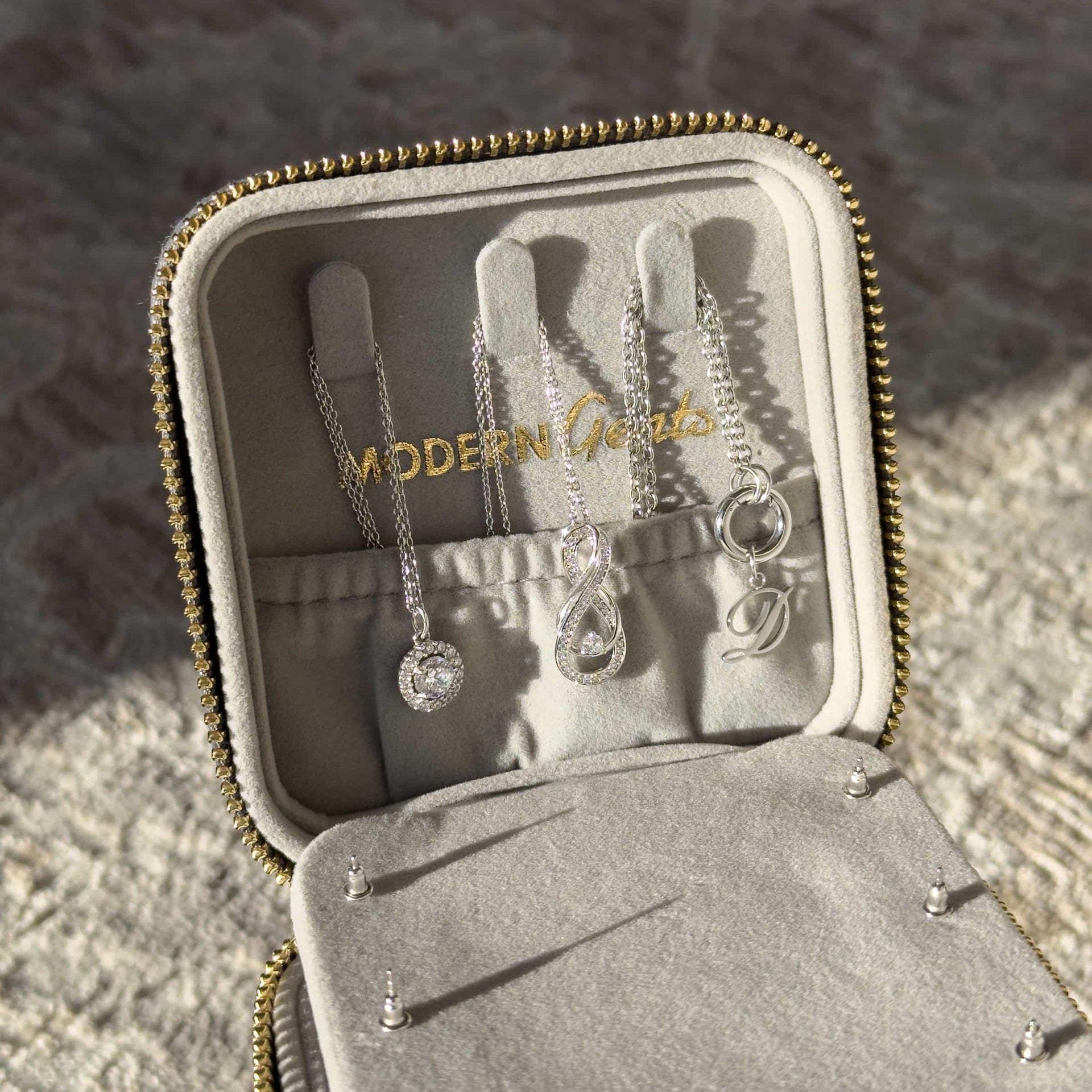 A charcoal color square shaped travel box with gold hardware opened from the top portion to showcase the hidden compartment for additional jewelry storage and the Modern Gents Logo