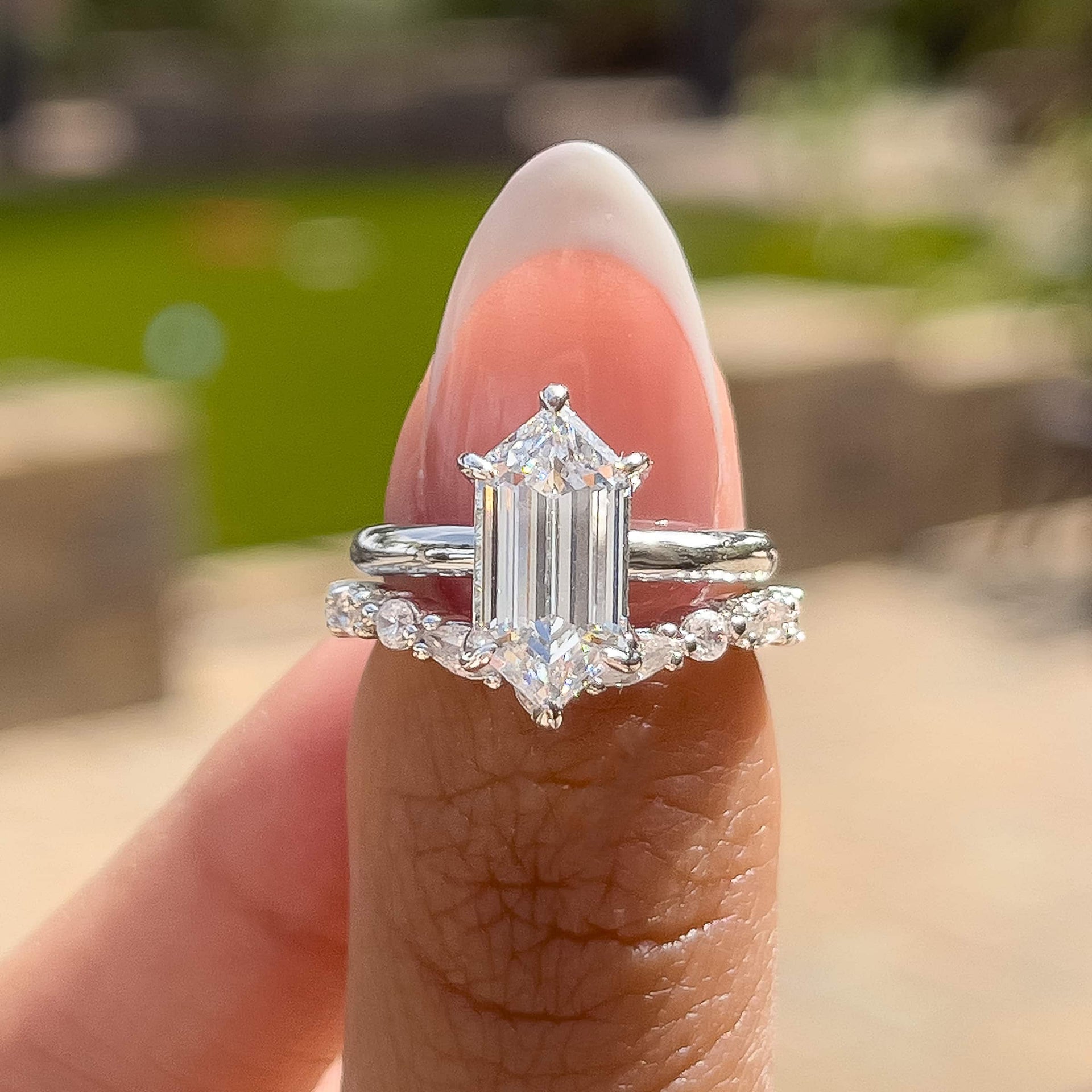 a stunningly unique silver 2.5 carat hexagon cut wedding ring set held by a model with french tip nails