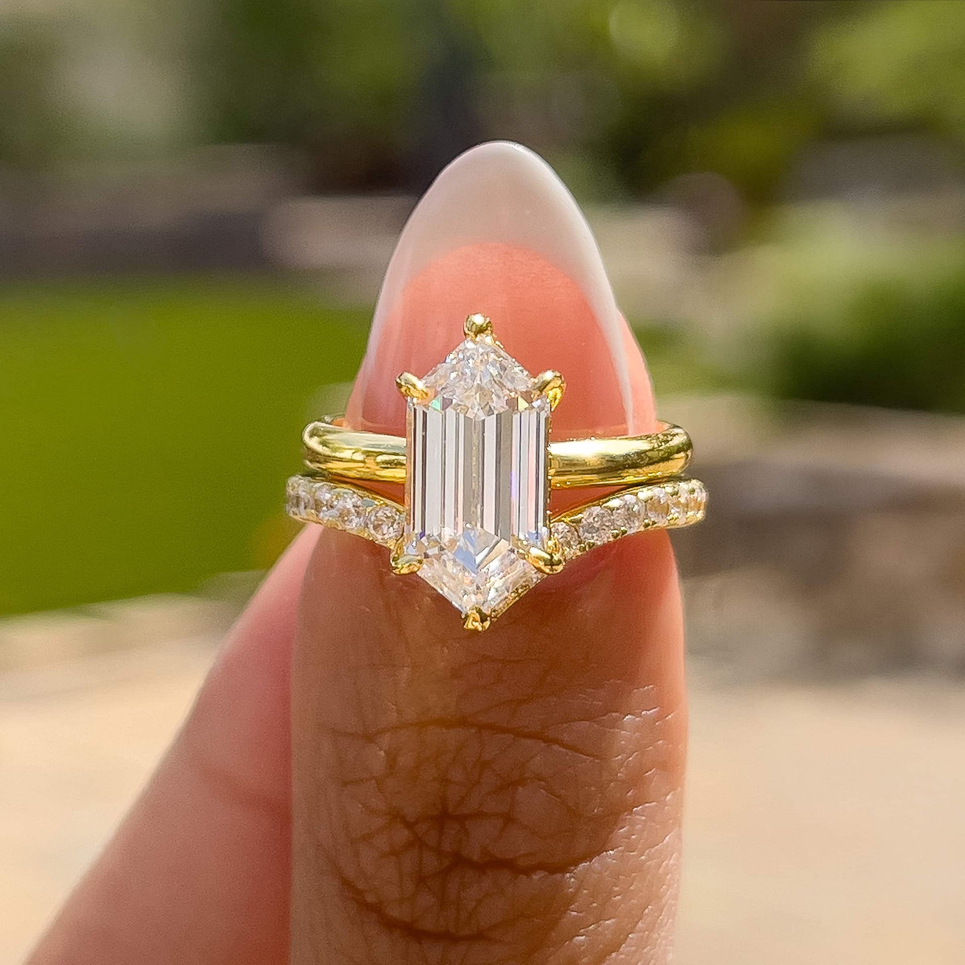 a stunning gold 2.5 carat hexagon cut solitaire, chevron band wedding ring set held by a model with french tip nails