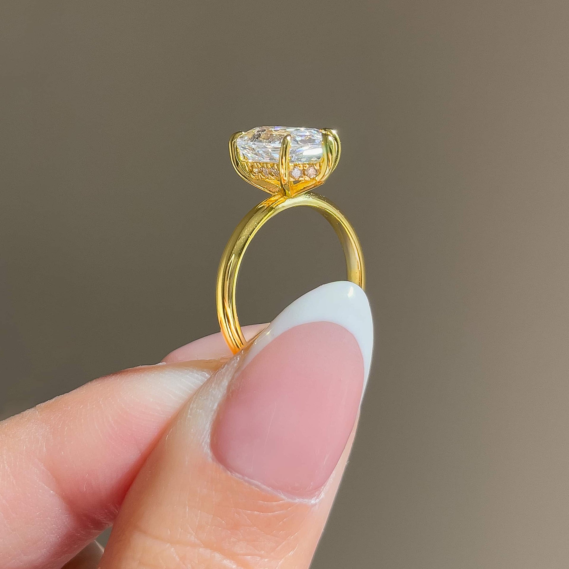side view of a gold 2.5 carat hexagon cut solitaire hidden halo engagement ring held by a model with french tip nails
