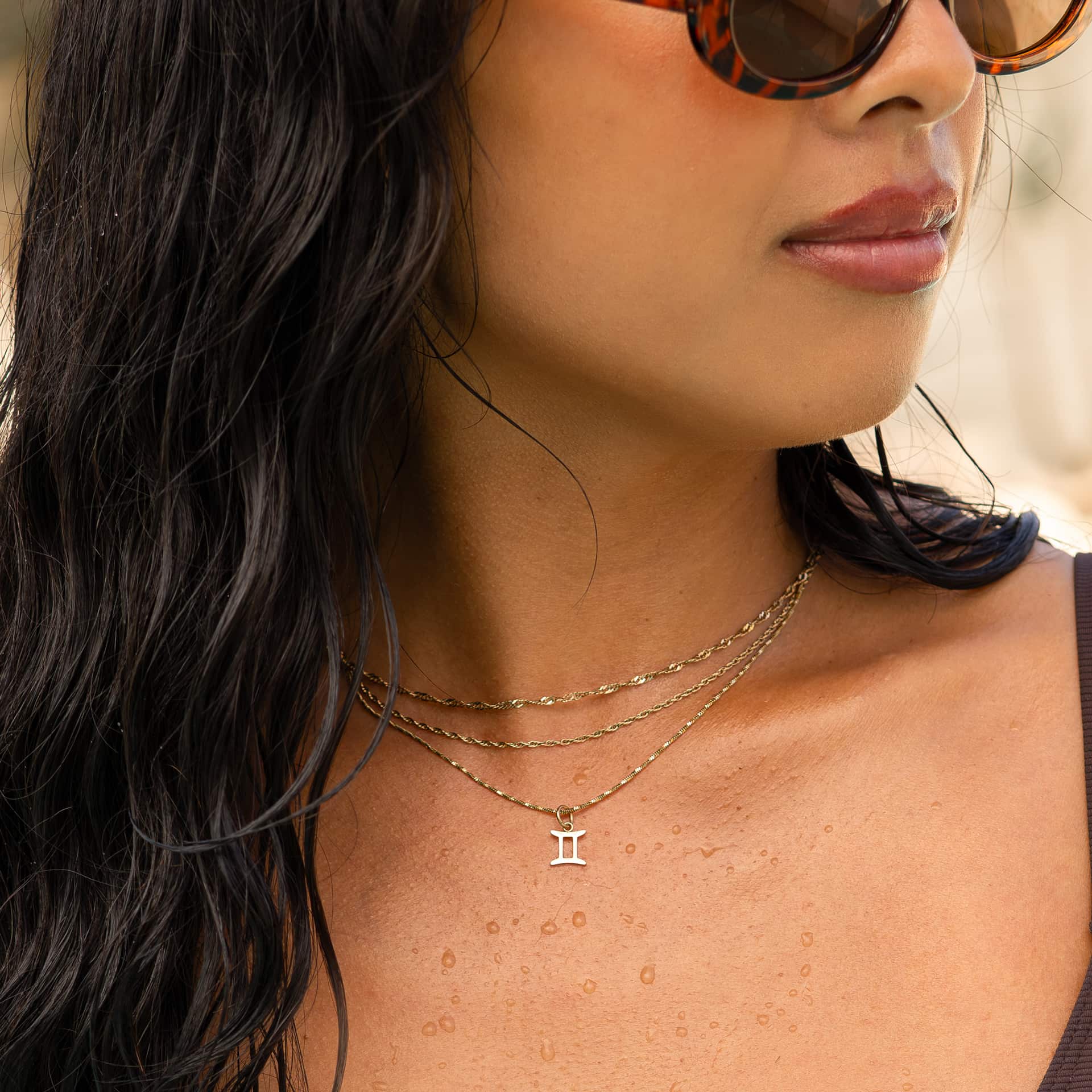 a dainty, 14k gold PVD plated stainless steel necklace stack featuring a zodiac charm worn by a model with dark hair and sunglasses