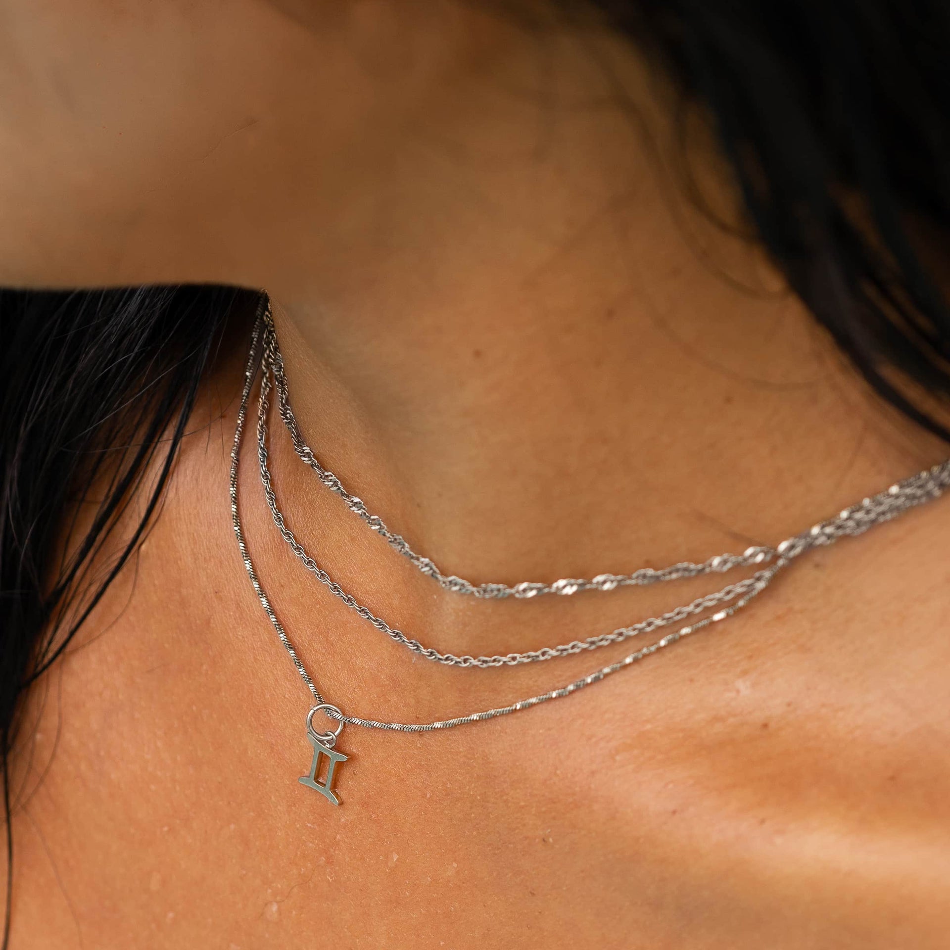 a dainty, silver stainless steel necklace stack featuring a zodiac charm worn by a model with dark hair