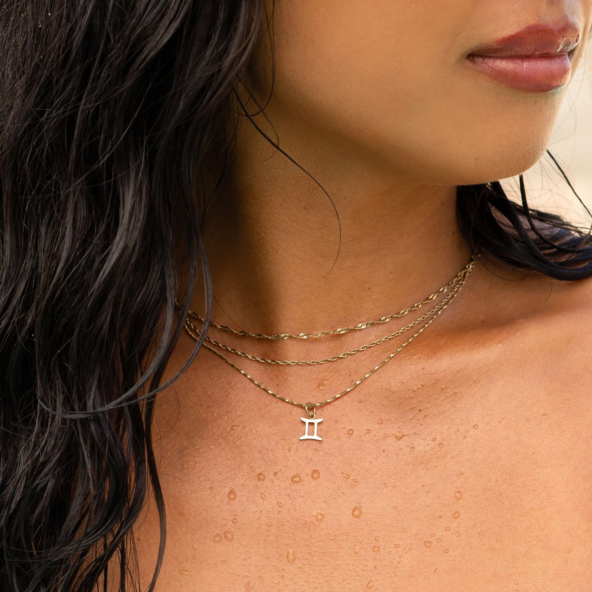 a dainty, 14k gold PVD plated stainless steel necklace stack featuring a zodiac charm worn by a model with dark hair 