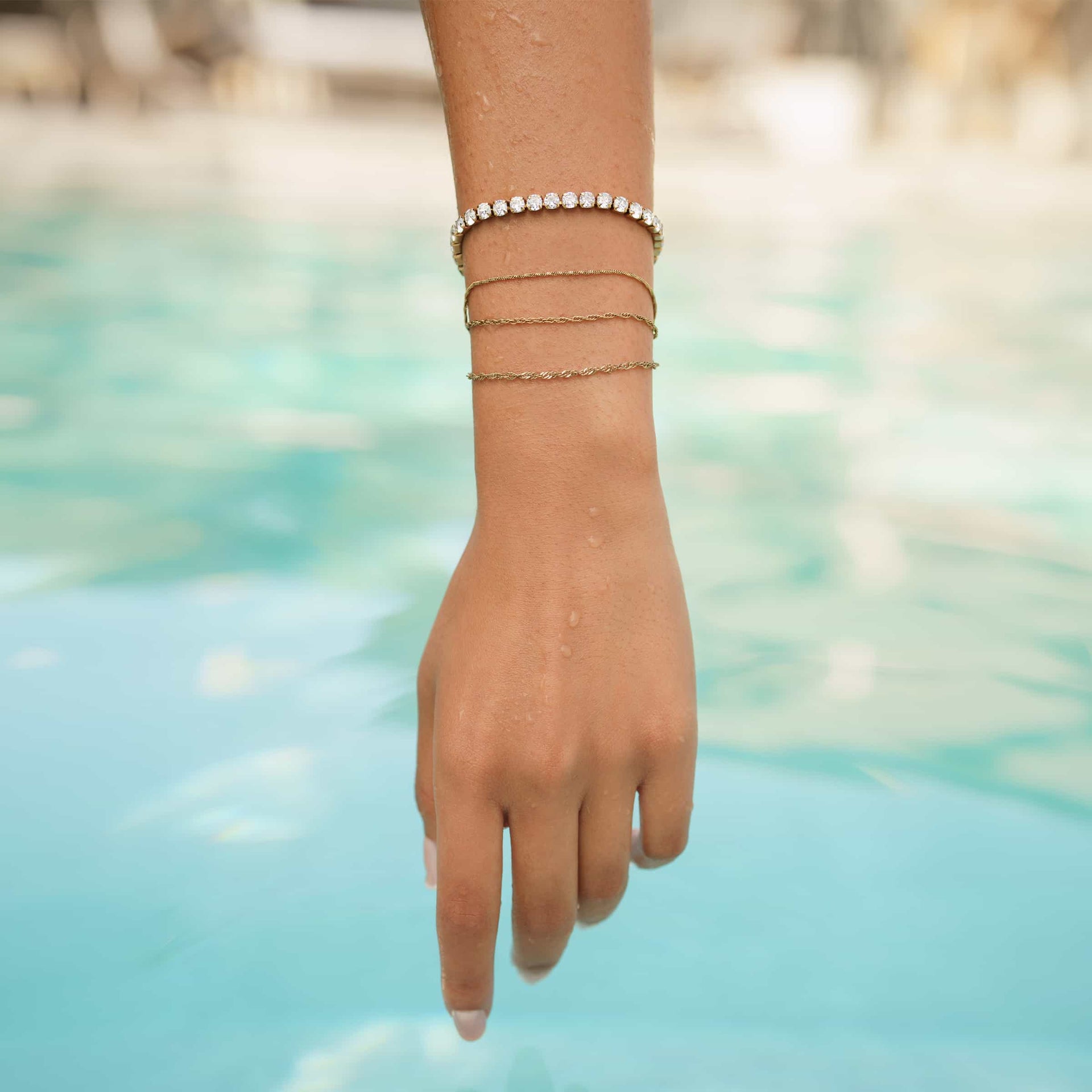 a 14k gold PVD plated stainless steel dainty bracelet stack worn by model at a pool