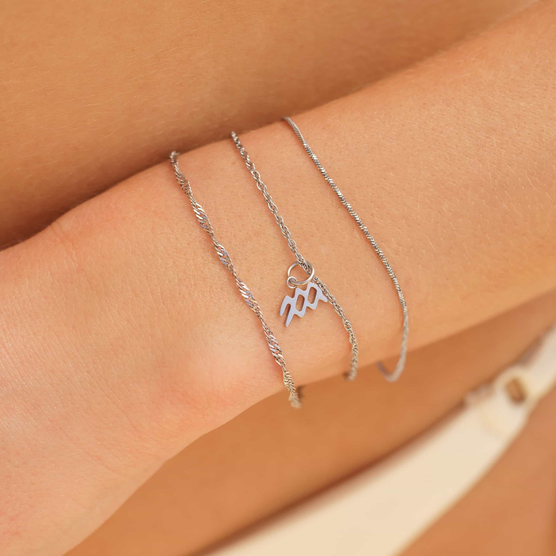 a silver stainless steel dainty bracelet stack with a zodiac charm detail worn by model in bikini