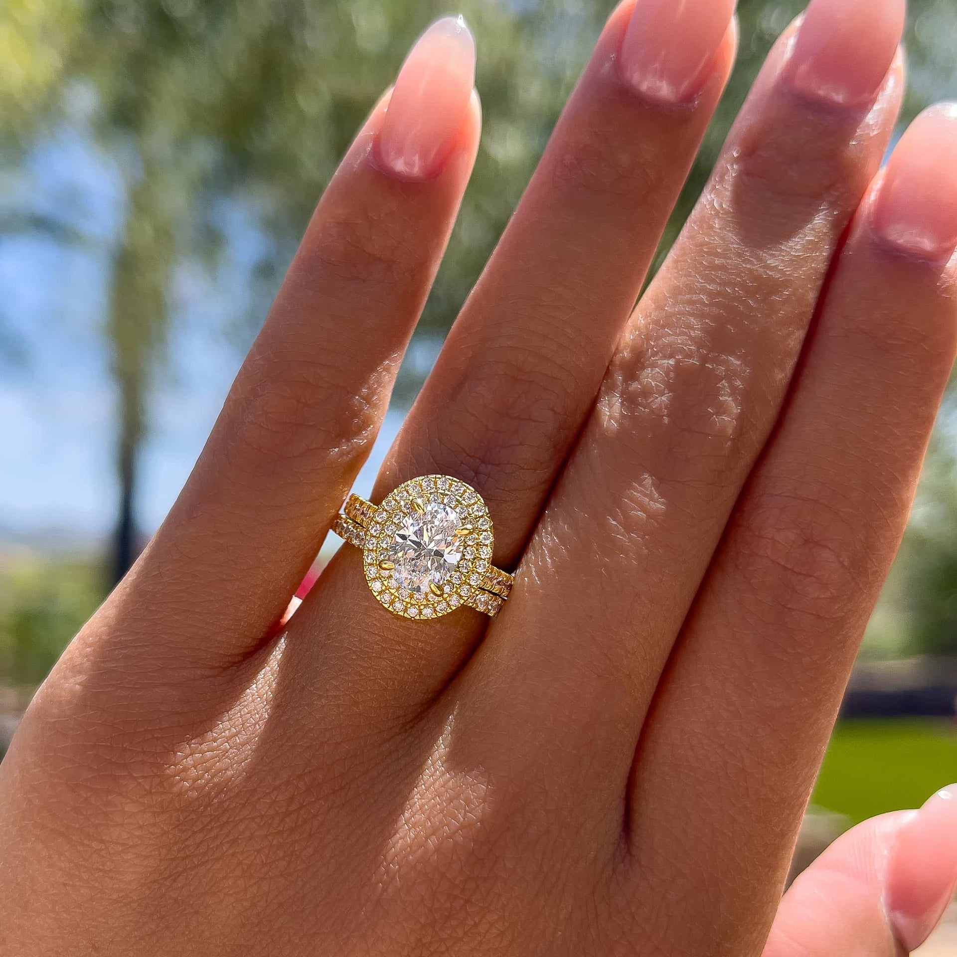 gold 1.5 carat oval cut half eternity wedding ring set worn by model with neutral colored nails outdoors